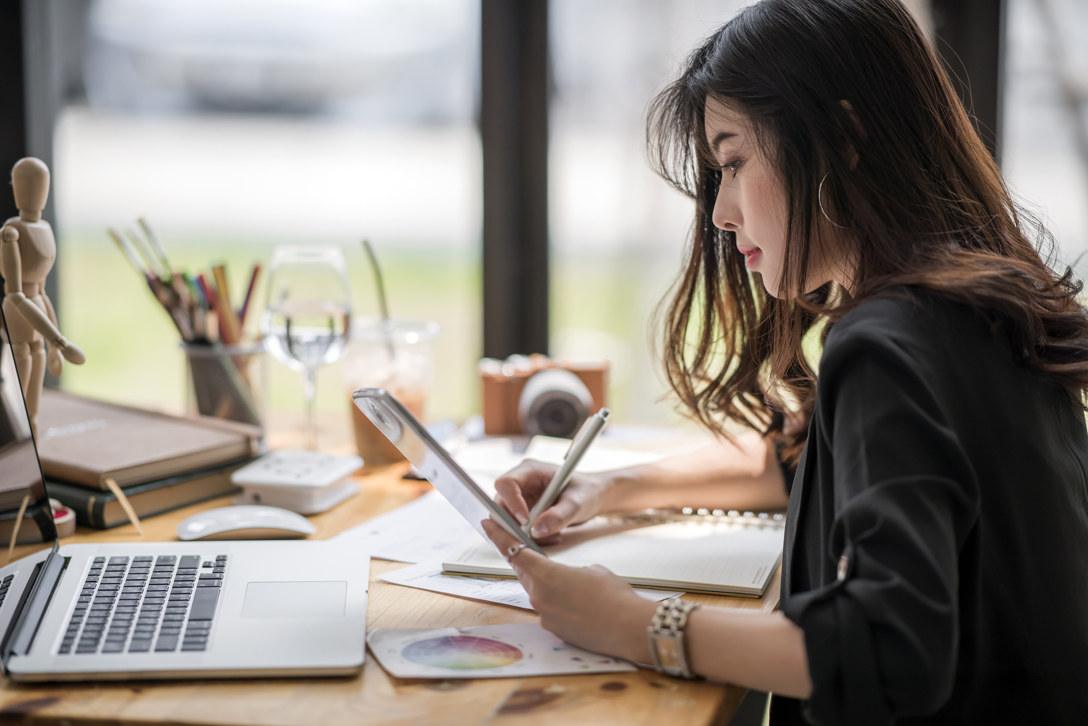 Female designer looking at tablet and writing note Designer looking at a tablet while writing a note.