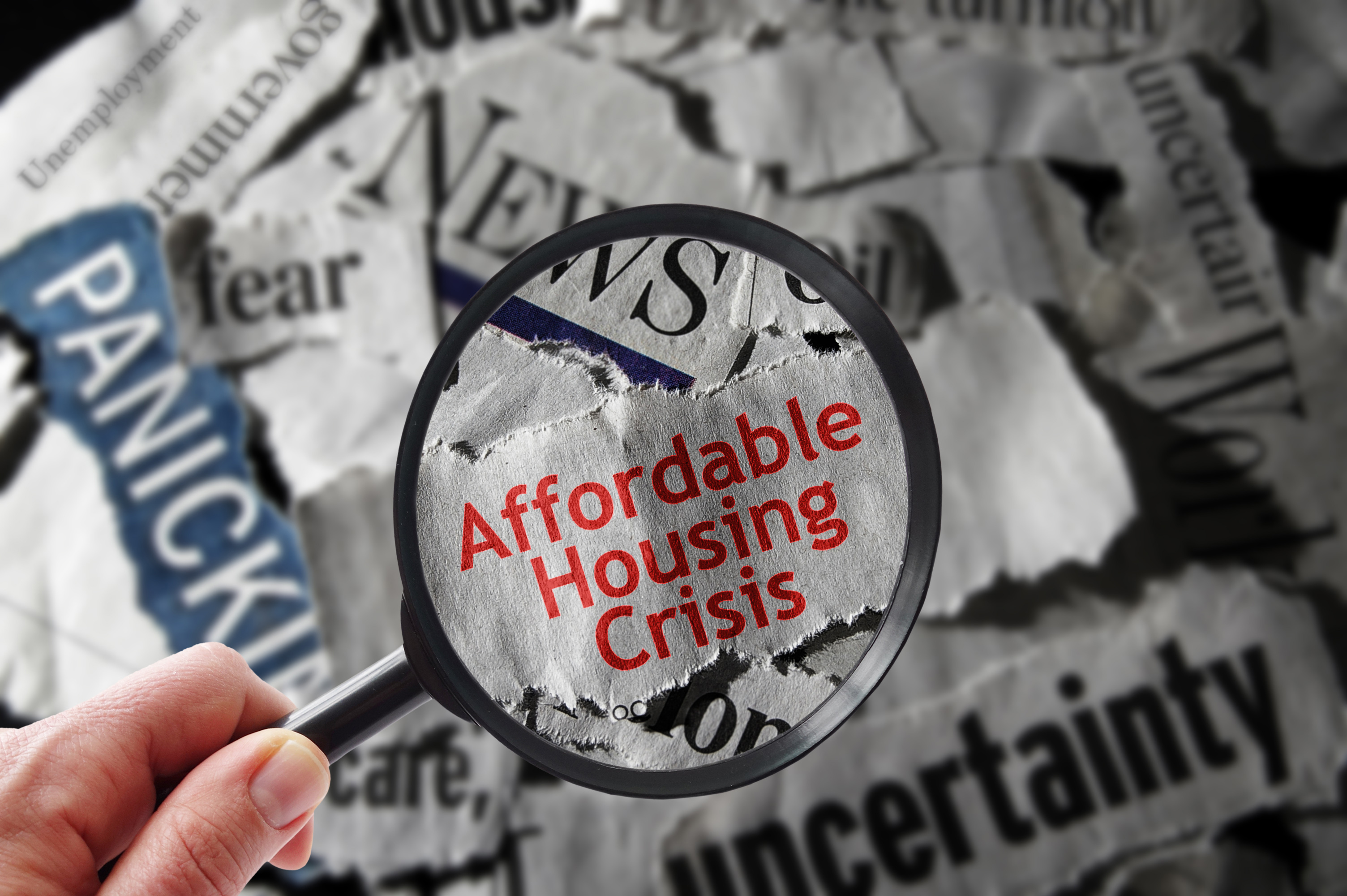 GettyImages-1002370532 Hands holding a magnifying glass over a slip of newspaper that says Affordable Housing.