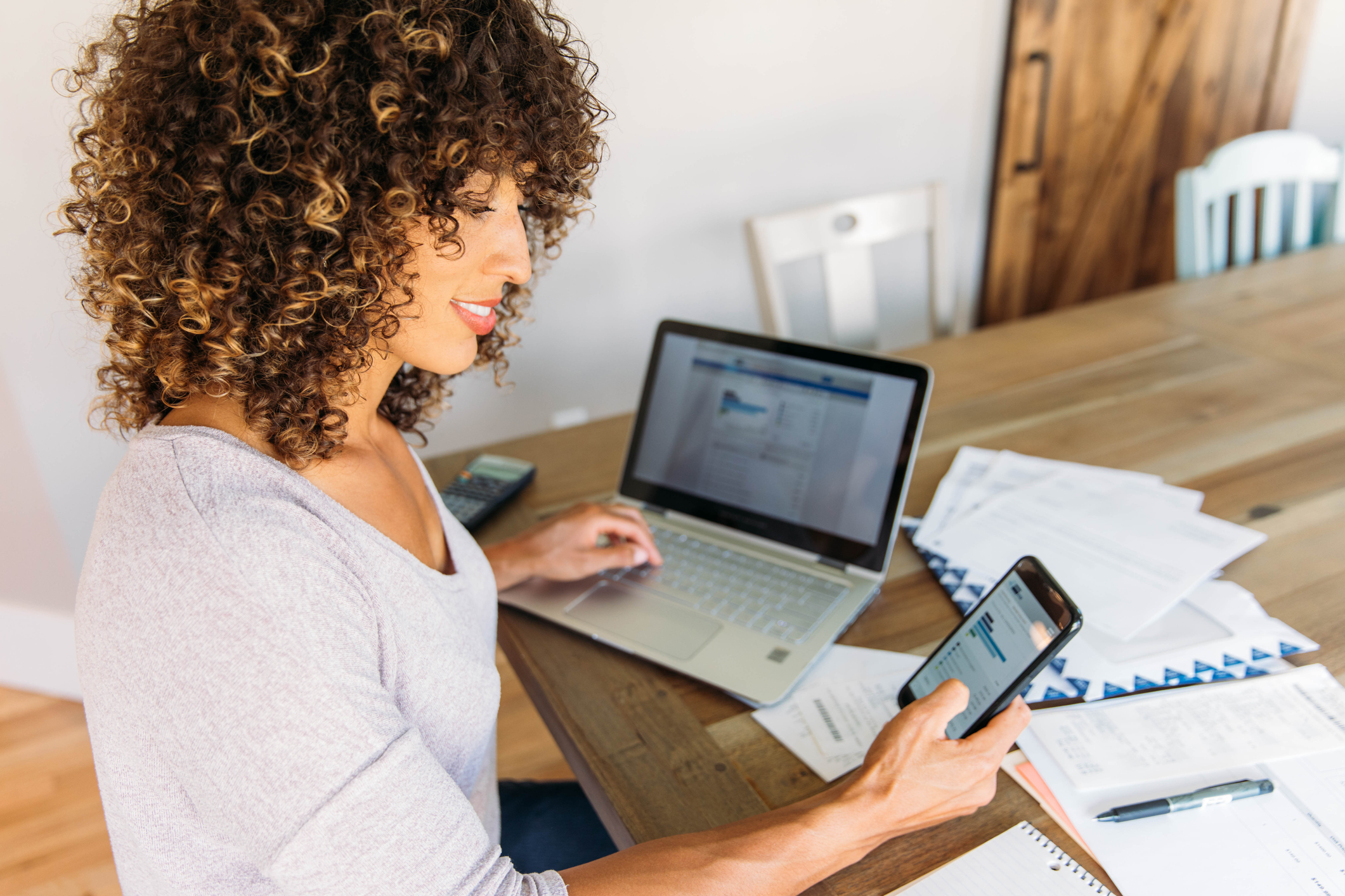 Person looking at online account Person working on laptop and cell phone with papers at desk.