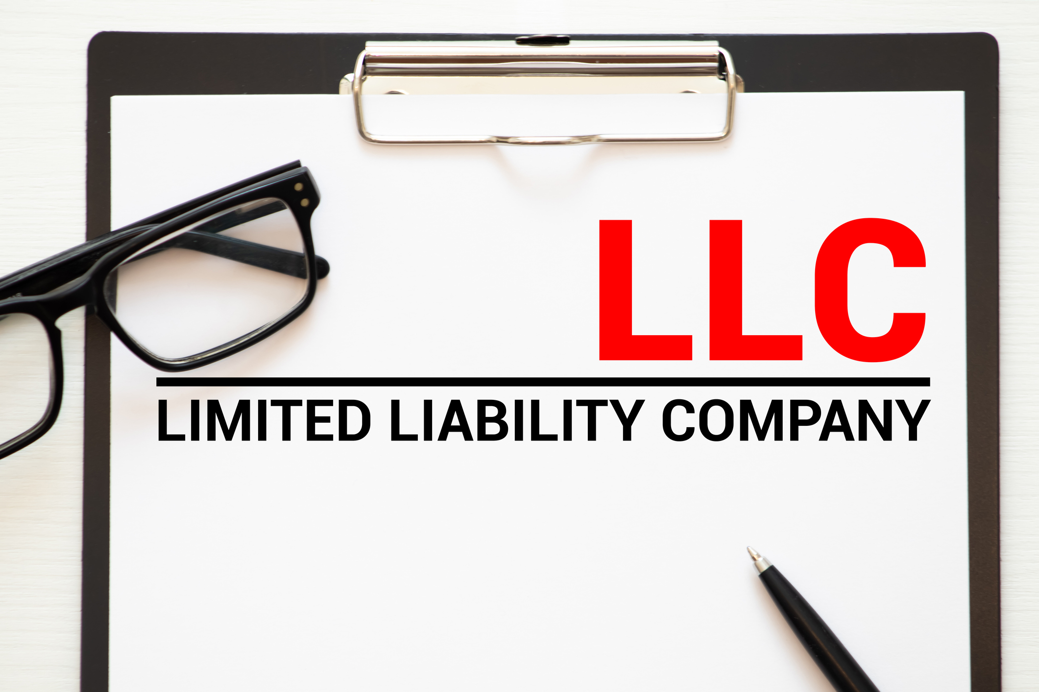 Clip board with paper and glasses and words LLC.jpg Clipboard with paper and glasses and the words Limited Liability Company, LLC.