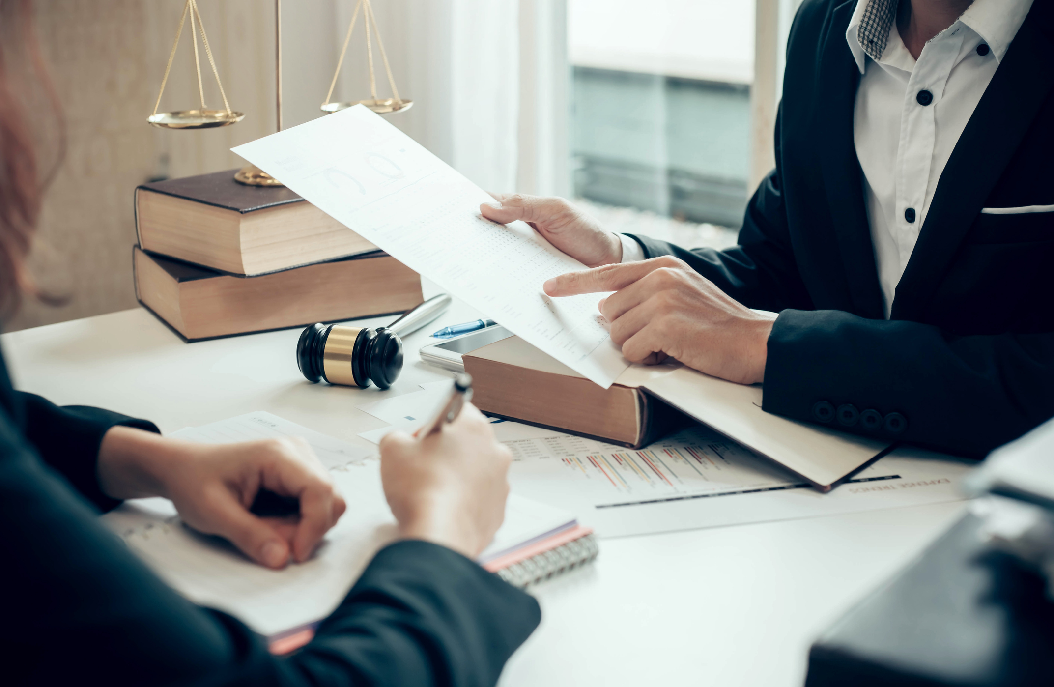 GettyImages-1287546532.jpg Two people talking and reading paperwork at desk with legal books and gavel.