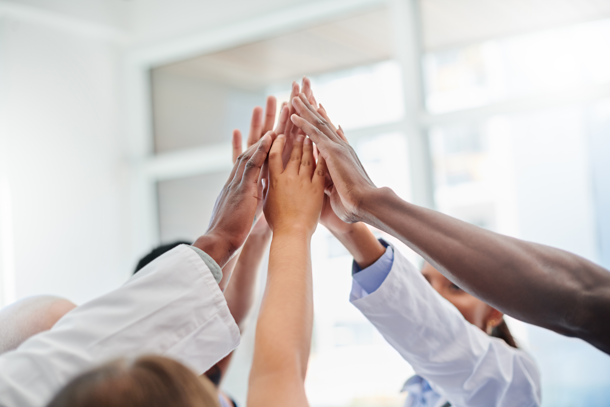 GettyImages-1324292384 People standing in a circle with their hands raised together in the middle.