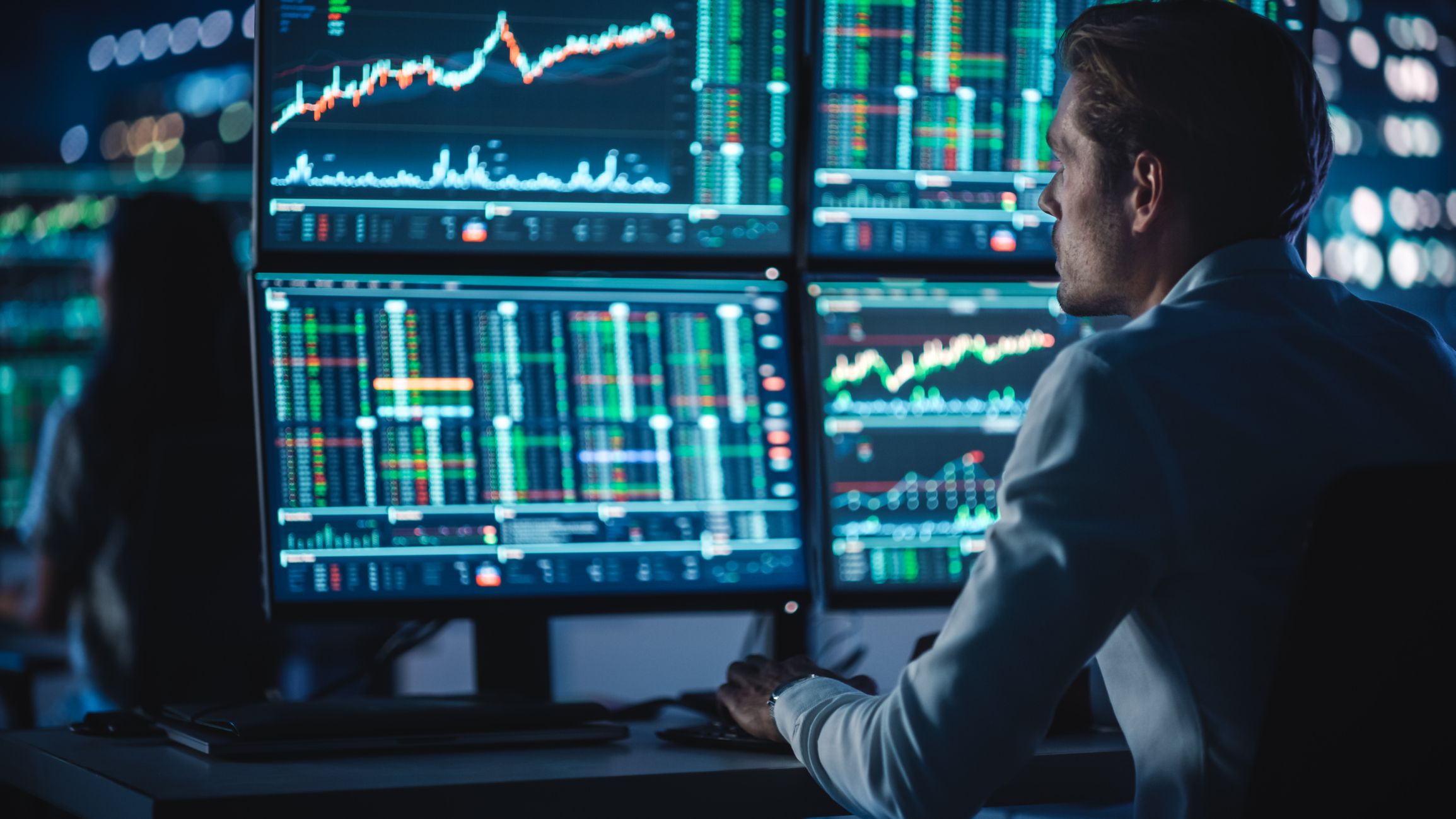 Investor in front of multiple monitors. An investor views charts and data on four monitors in an office.