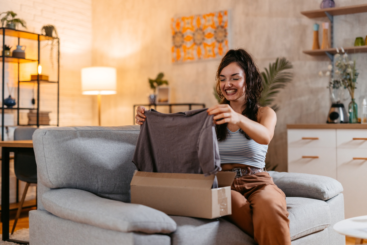 Smiling person holding up shirt from package Smiling person holding up a shirt from inside a package.