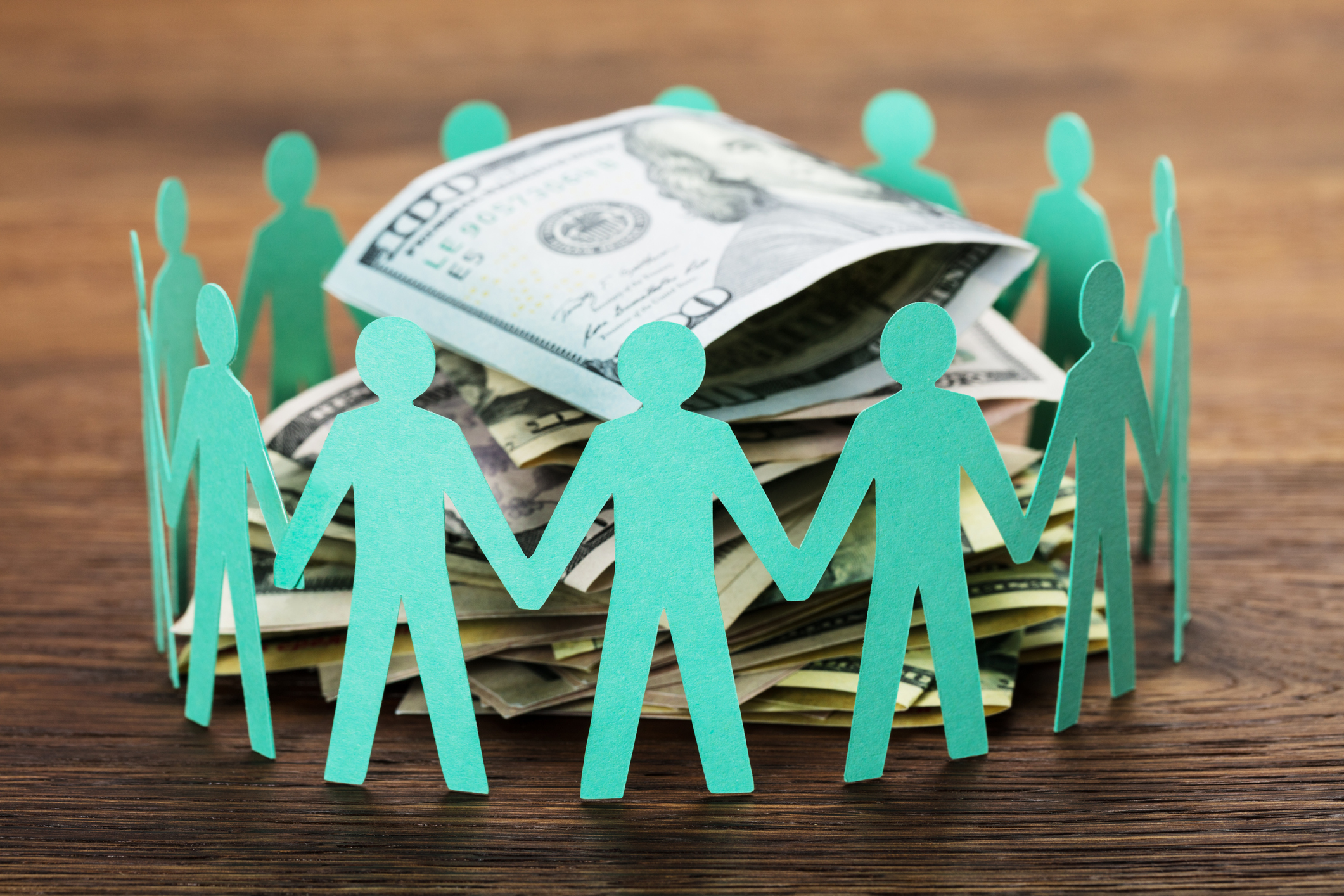 Green paper cut-outs of people holding hands around a pile of money. Green paper cut-outs of people holding hands around a pile of money.