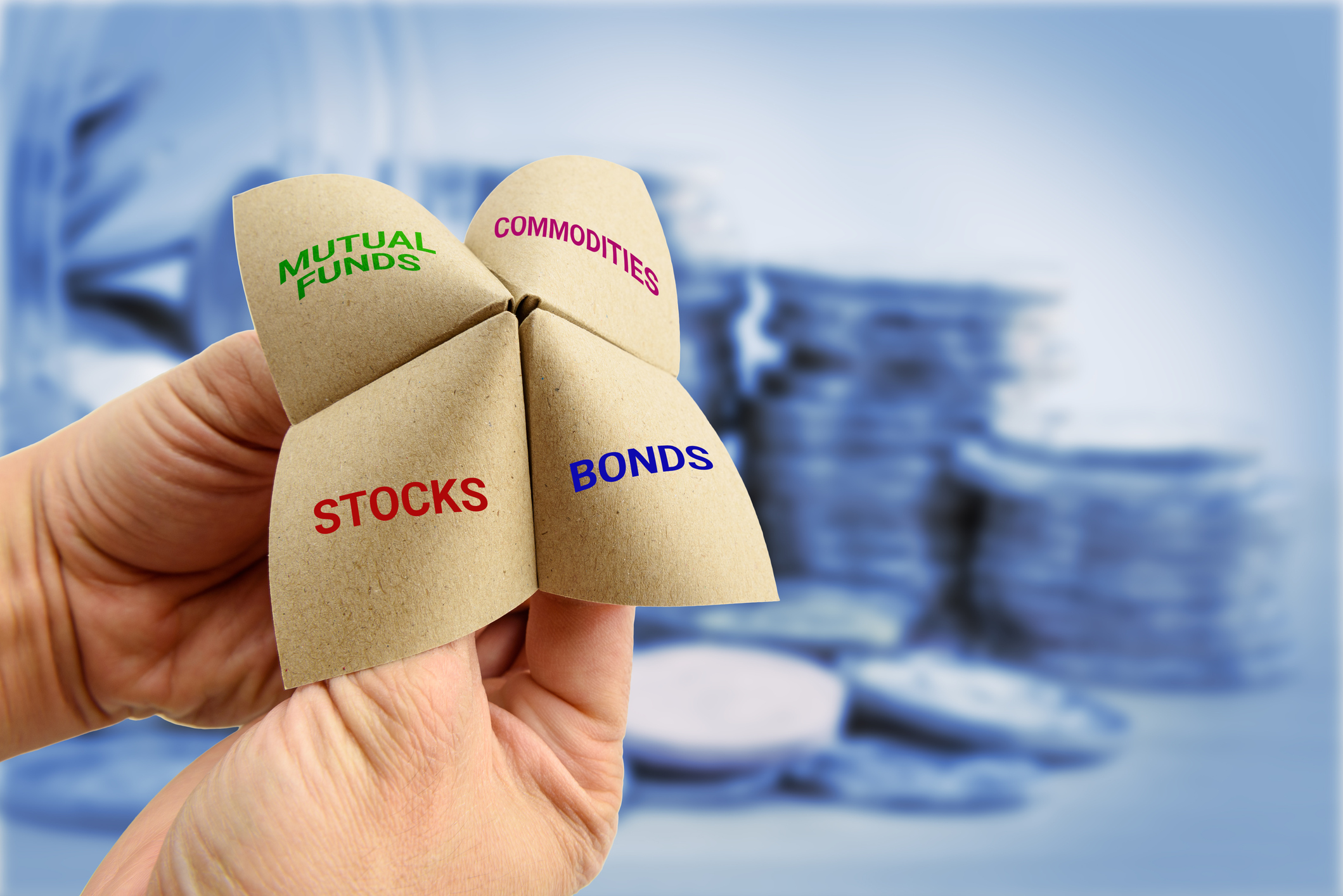 Asset allocation categories - stocks, bonds, etc. Hands playing a child's game with a folded paper labeled Stocks, Bonds, Commodities, and Mutual Funds.