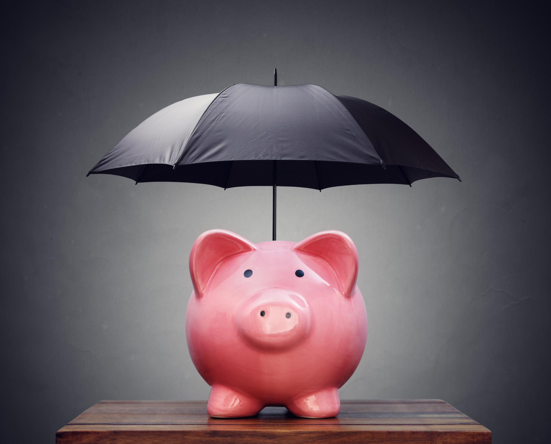 A piggy bank has a black umbrella open above it. A piggy bank has a black umbrella open above it.