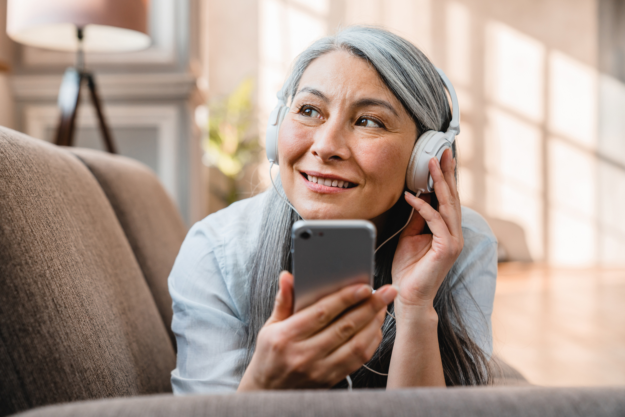 Getty - listening to phone podcast music Person listening to their phone and smiling.