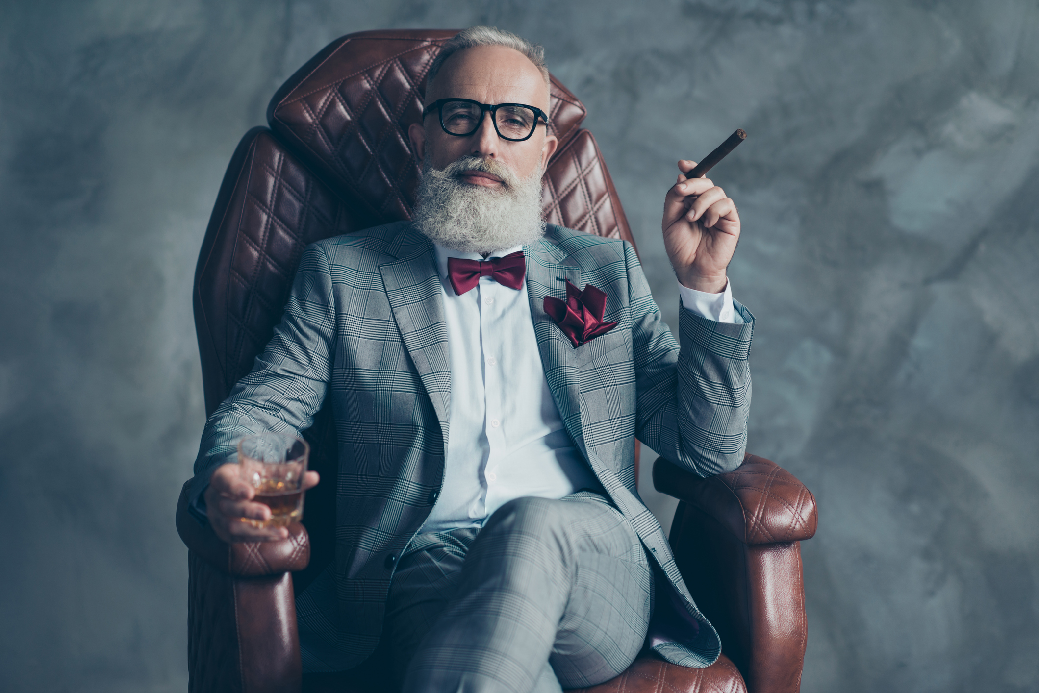 rich person with cigar wealthy millionaire success style A person in a suit is holding a cigar while seated in an expensive-looking leather chair.