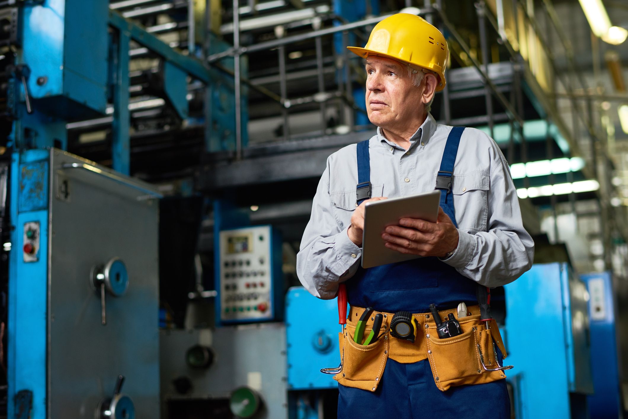 Person wearing construction hat and holding clipboard in factory.