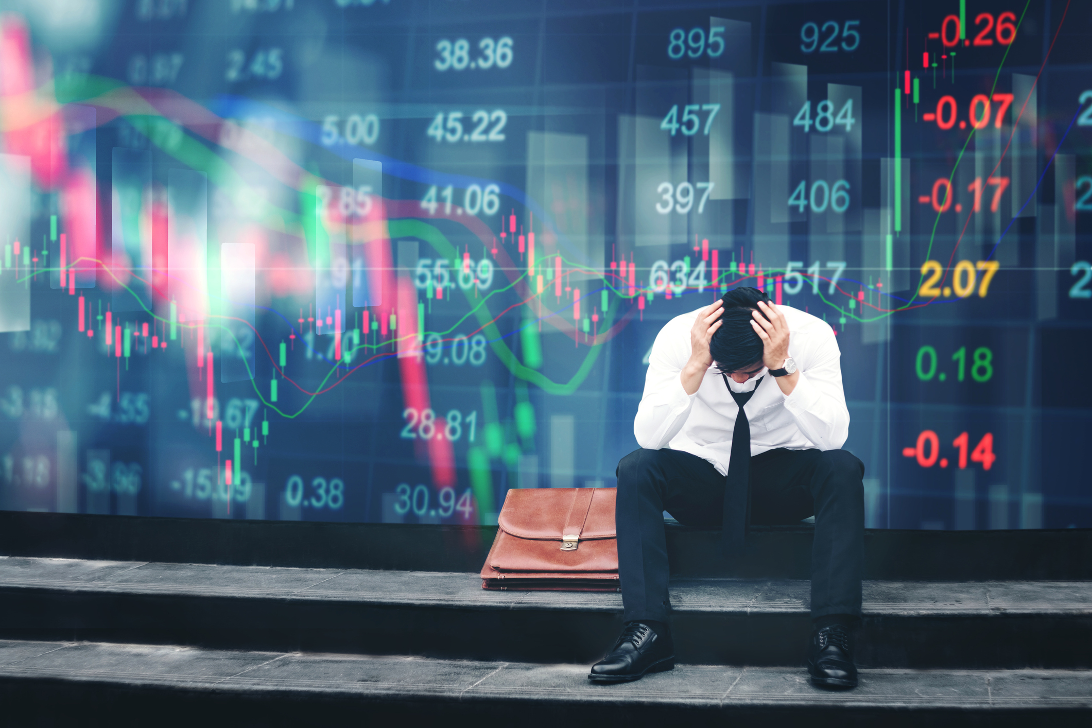 An upset investor sits in front of a screen showing plunging stock prices. An upset investor sits in front of a large screen showing plunging stock prices.