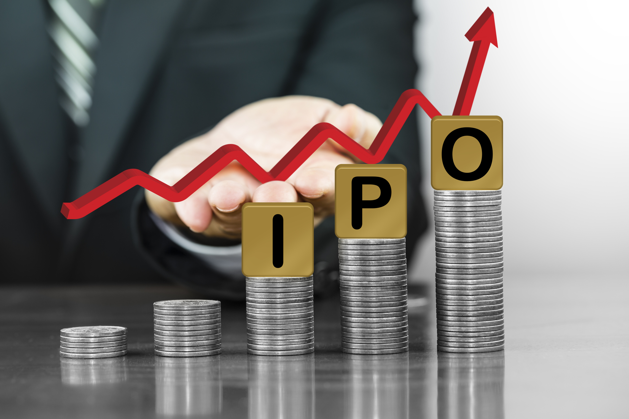 Arrow rising over the word IPO and coins. Arrow rising over blocks spelling out the letters IPO sitting atop stacks of coins.