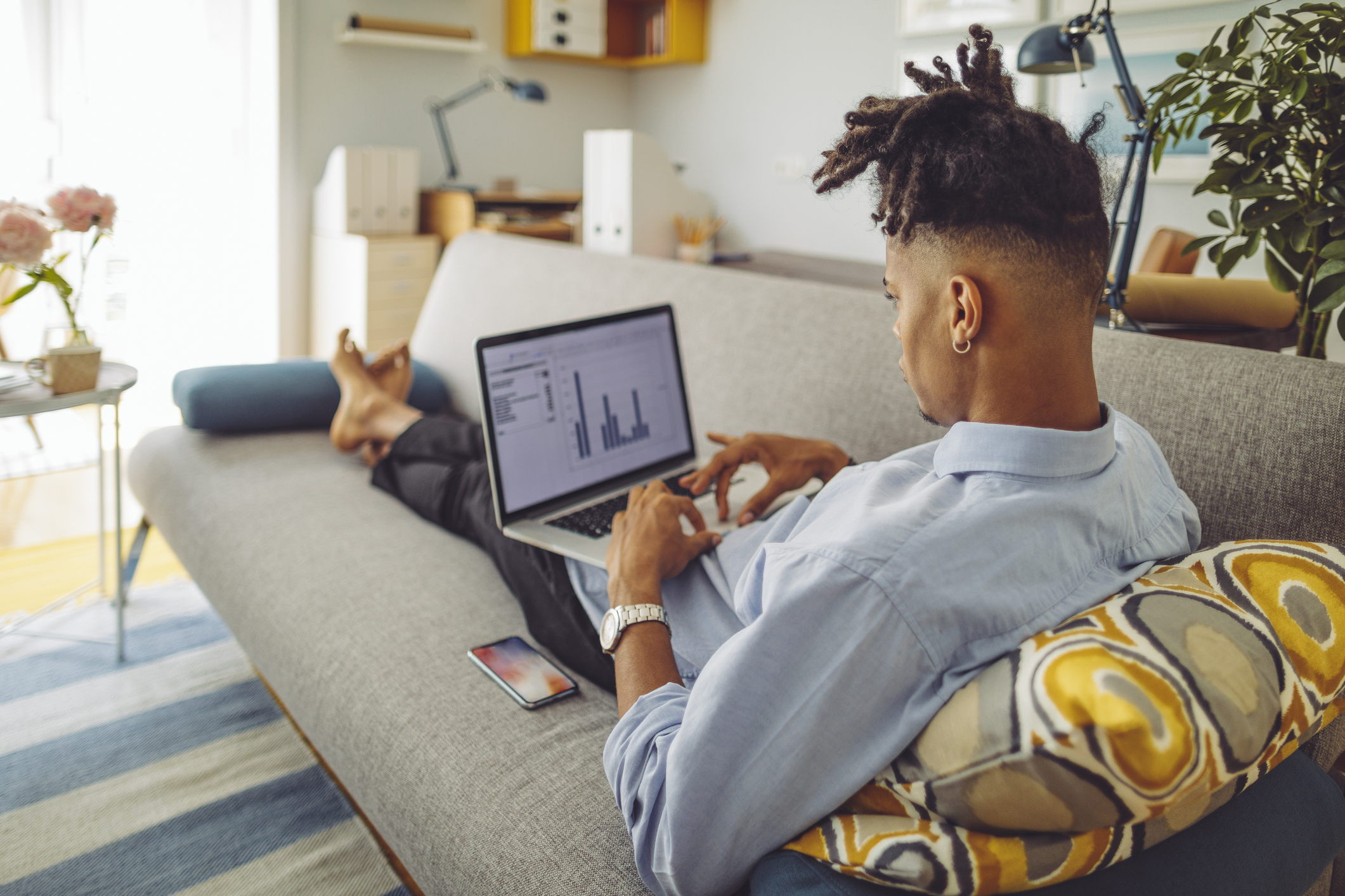 Investor lying on couch with laptop open to charts. Person lying on couch with laptop screen showing charts.