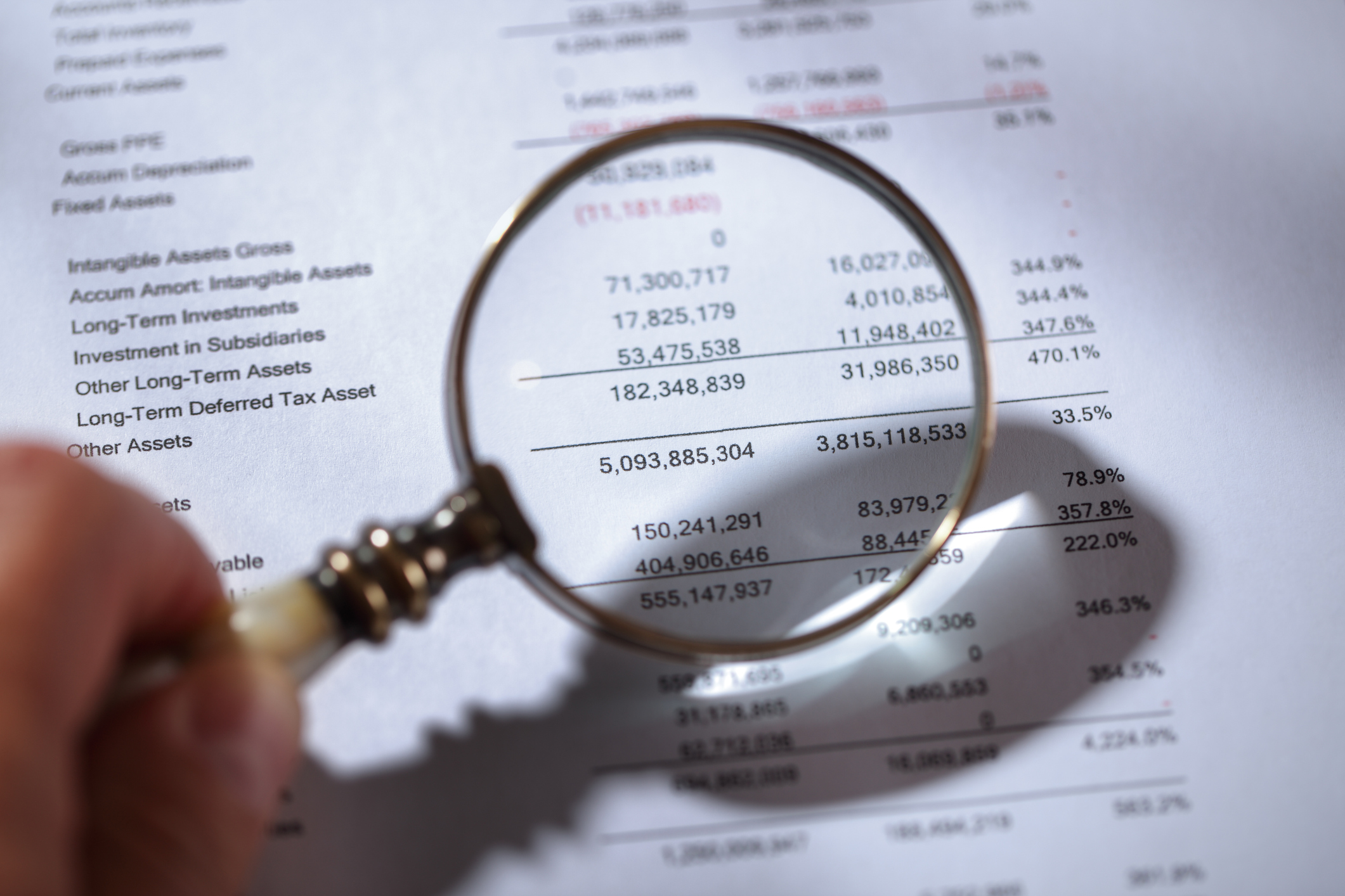 Looking at financials with magnifying glass A hand holding a magnifying glass up to some financial statements.