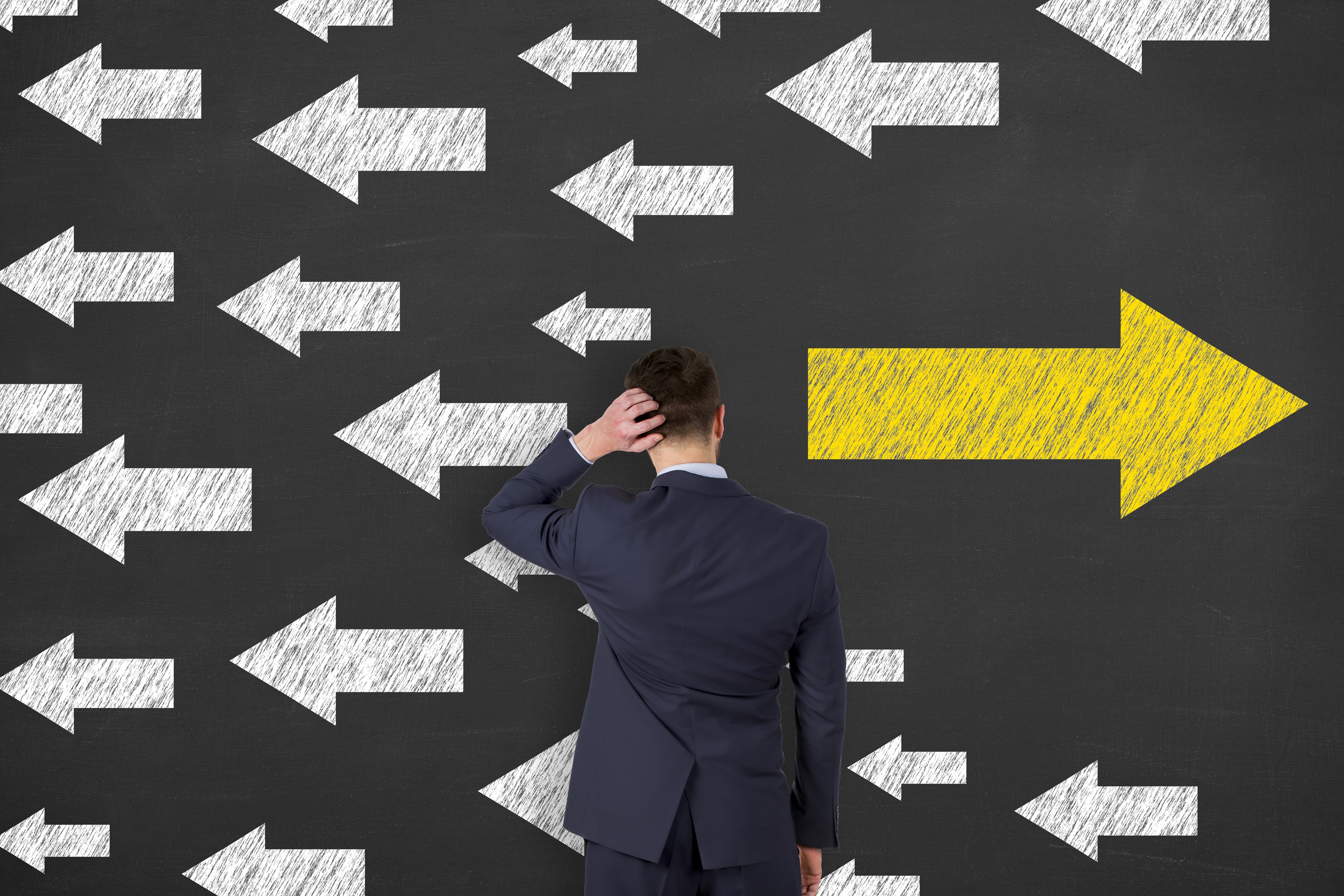 Man stands in front of boards with a bunch of white arrows pointing left and one larger yellow arrow pointing right.