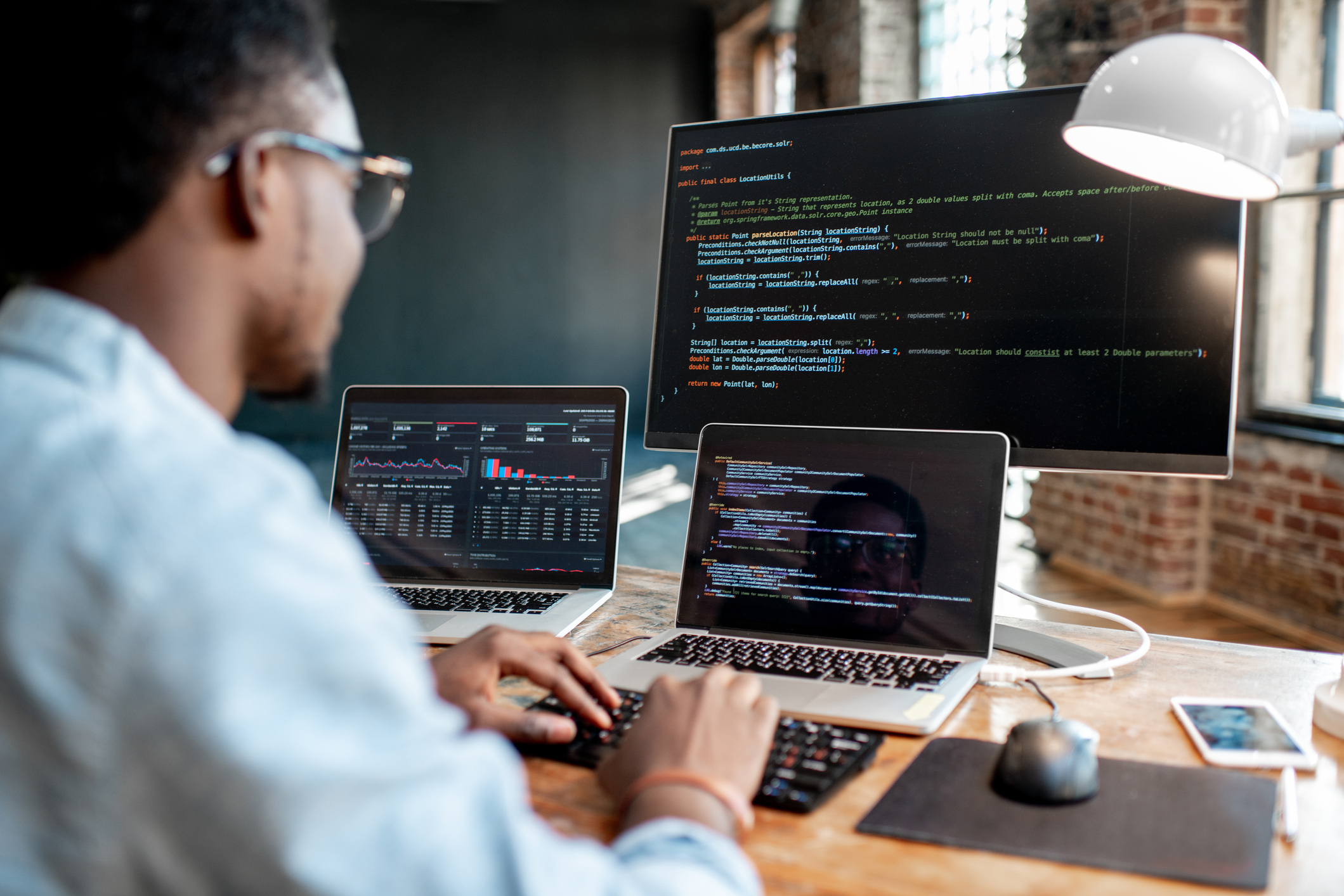 Software engineer typing on laptop with multiple screens in front of him.