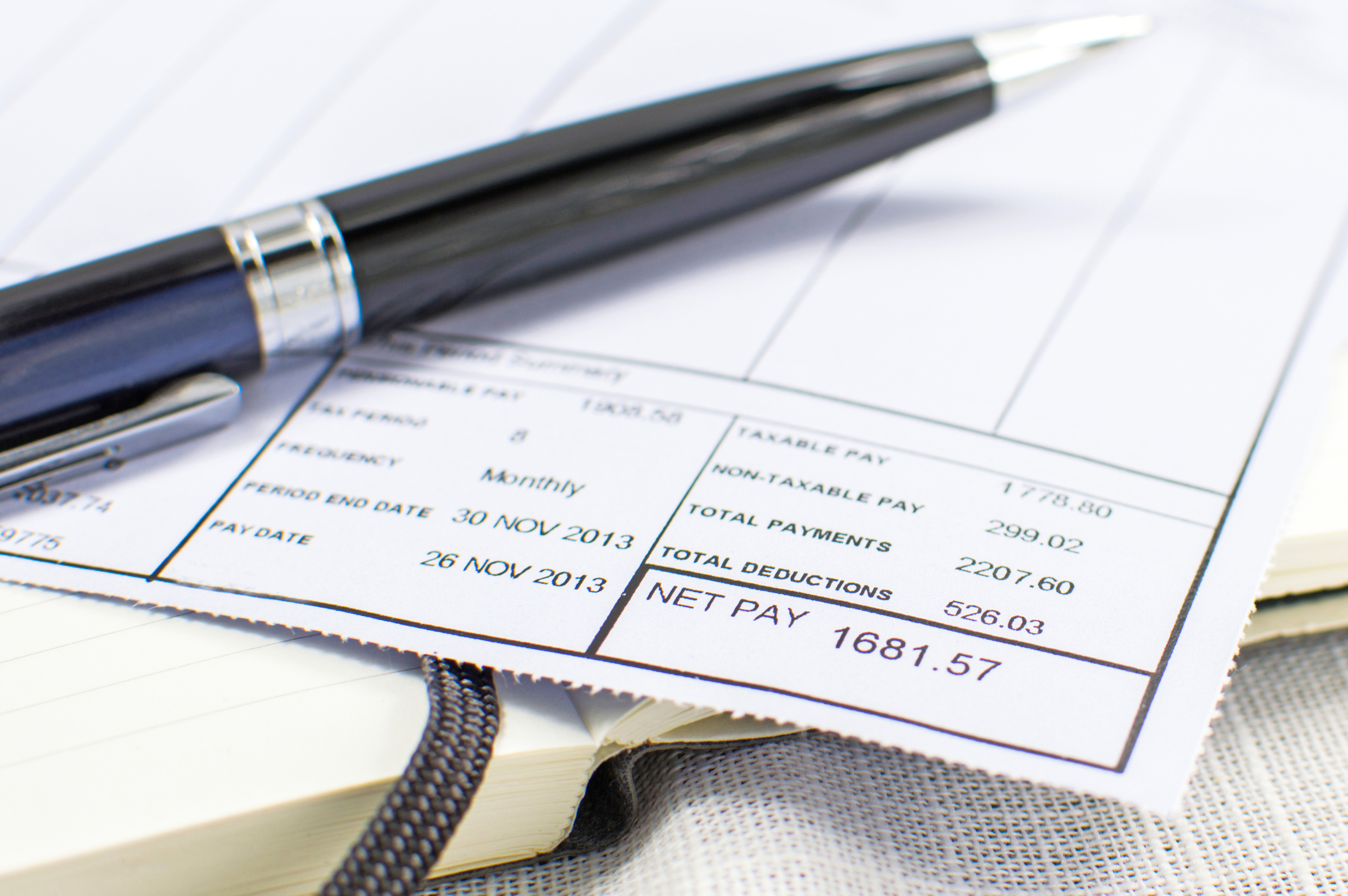 A close-up of a pay stub with a pen lying on top of it.