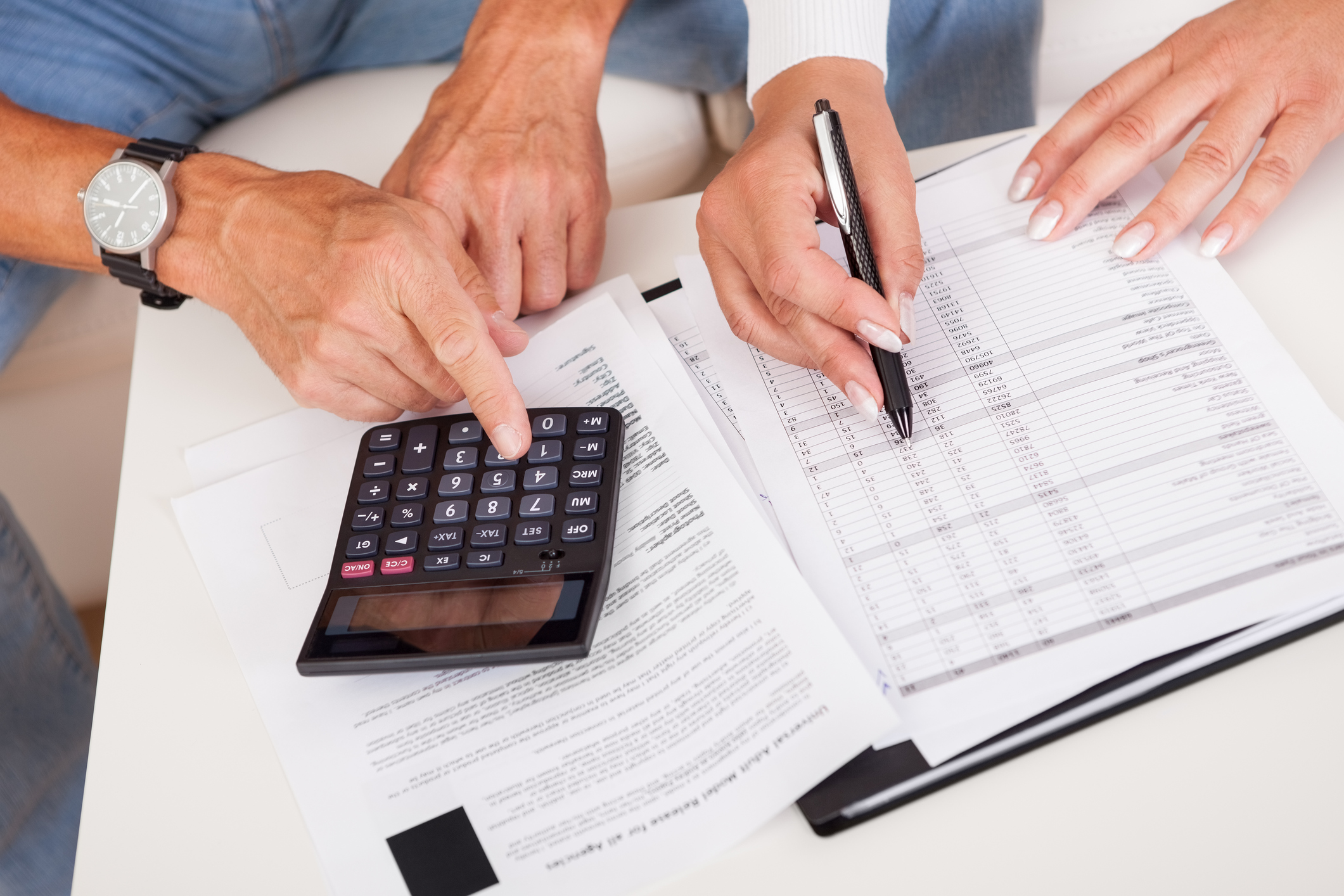 Two people doing paperwork with pen and calculator.