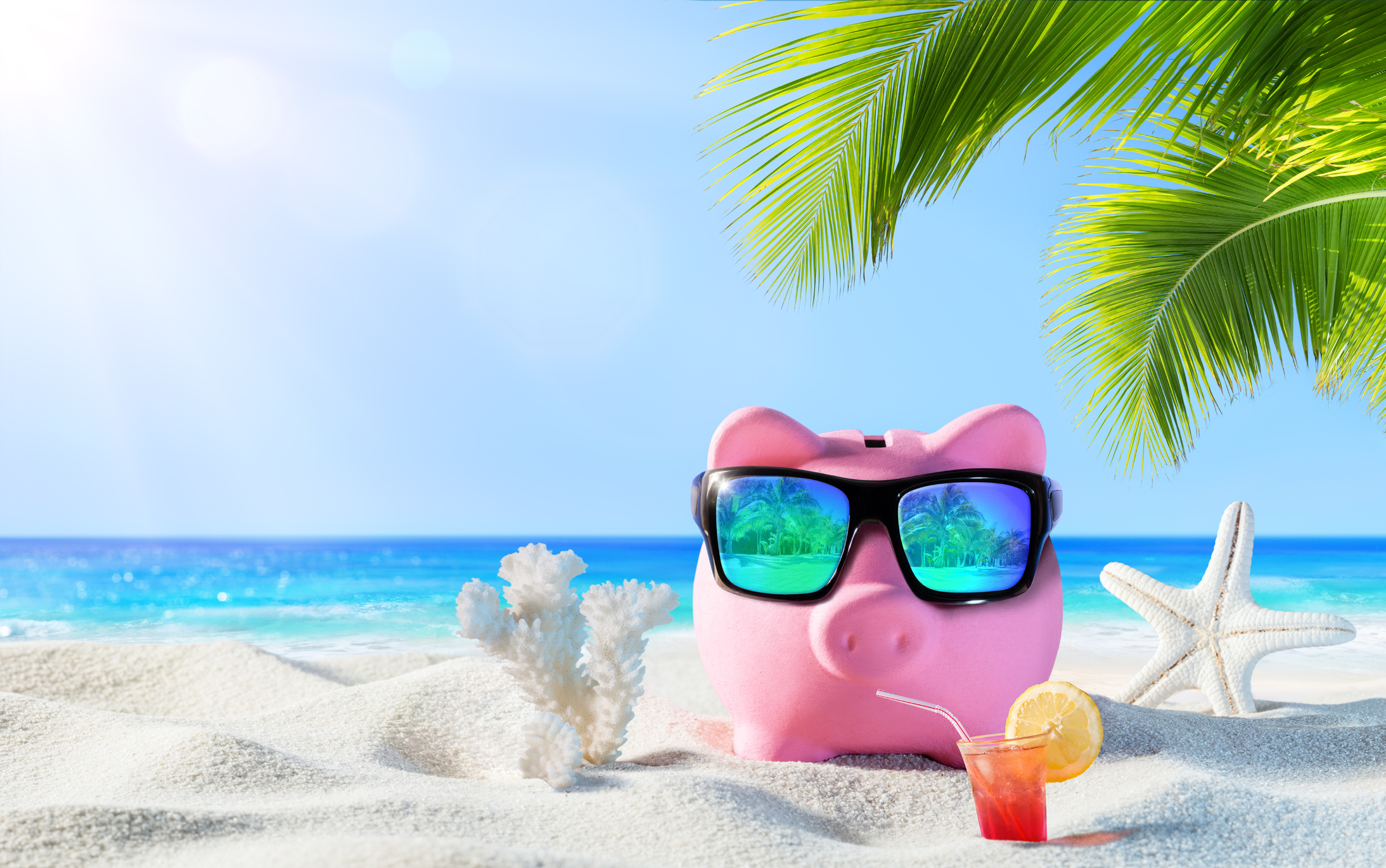Piggy bank with a drink and sunglasses on the beach.