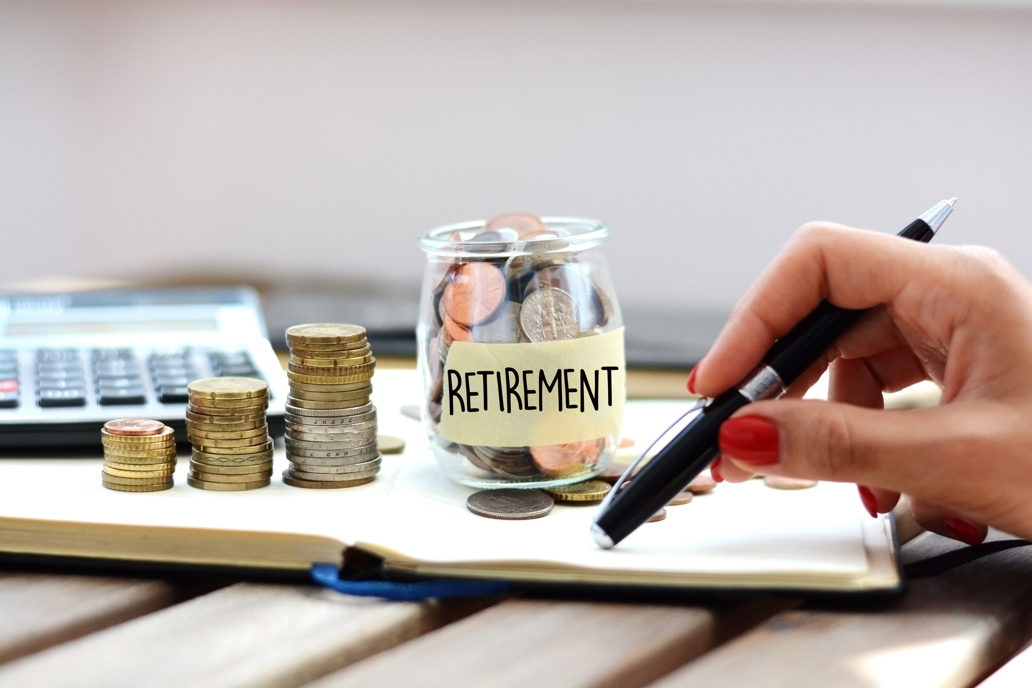 Retirement savings Hand holds pen near jar of coins labeled Retirement.