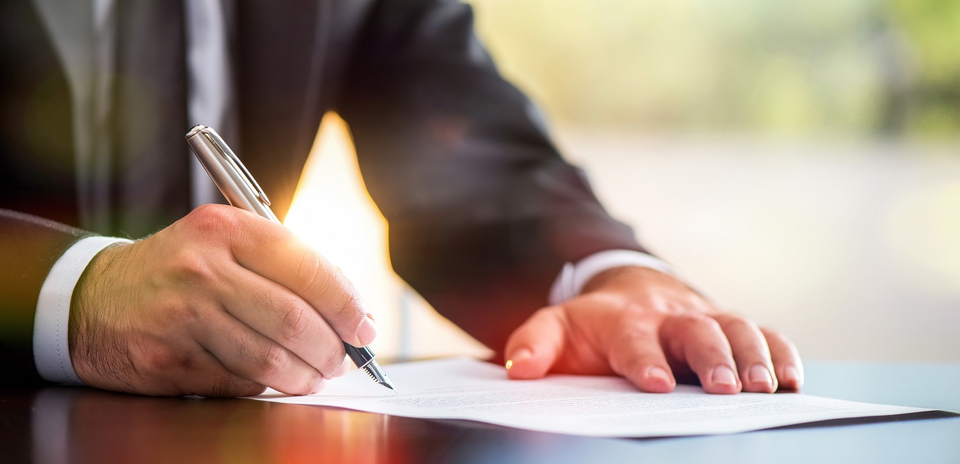 Man in business suit signs his signature to paperwork Person in business suit signs paperwork.