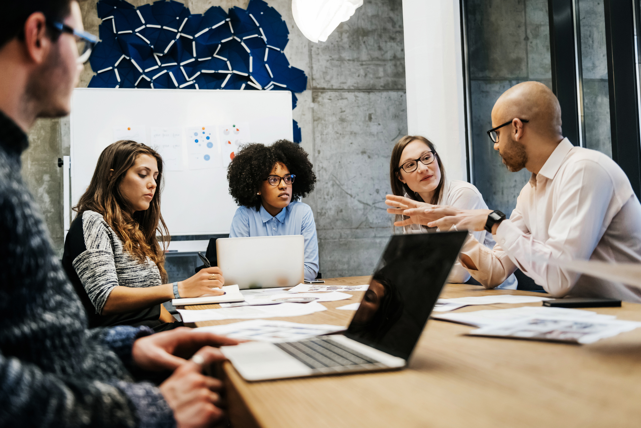 Businesspeople sitting at conference table with laptops and paperwork out conducting work meeting. Businesspeople sitting at conference table with laptops and paperwork out conducting work meeting.