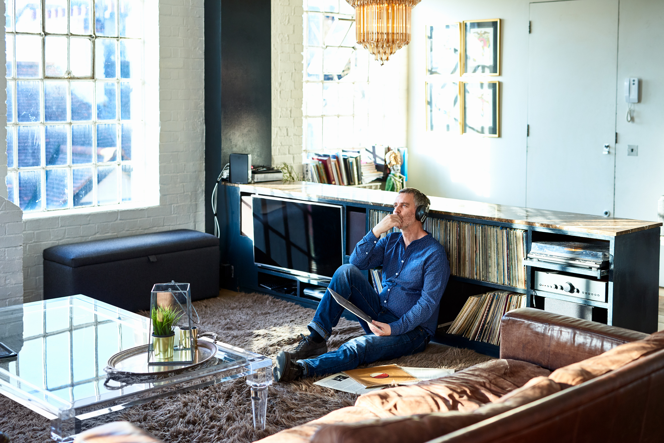 Person sitting on floor of sunny apartment and listening to music through headphones.