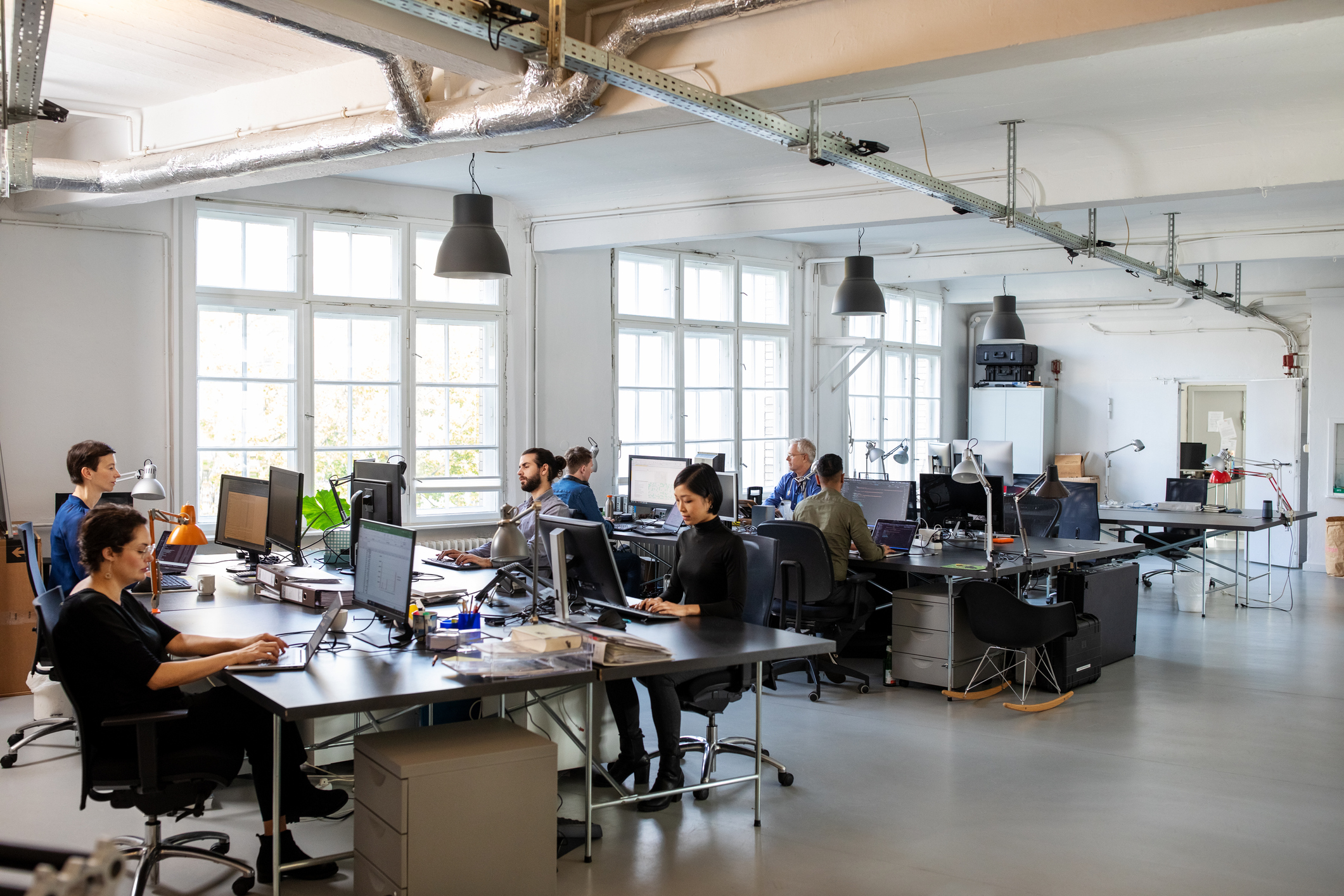 Workers sitting at desks in trendy office setting with large windows and high ceilings