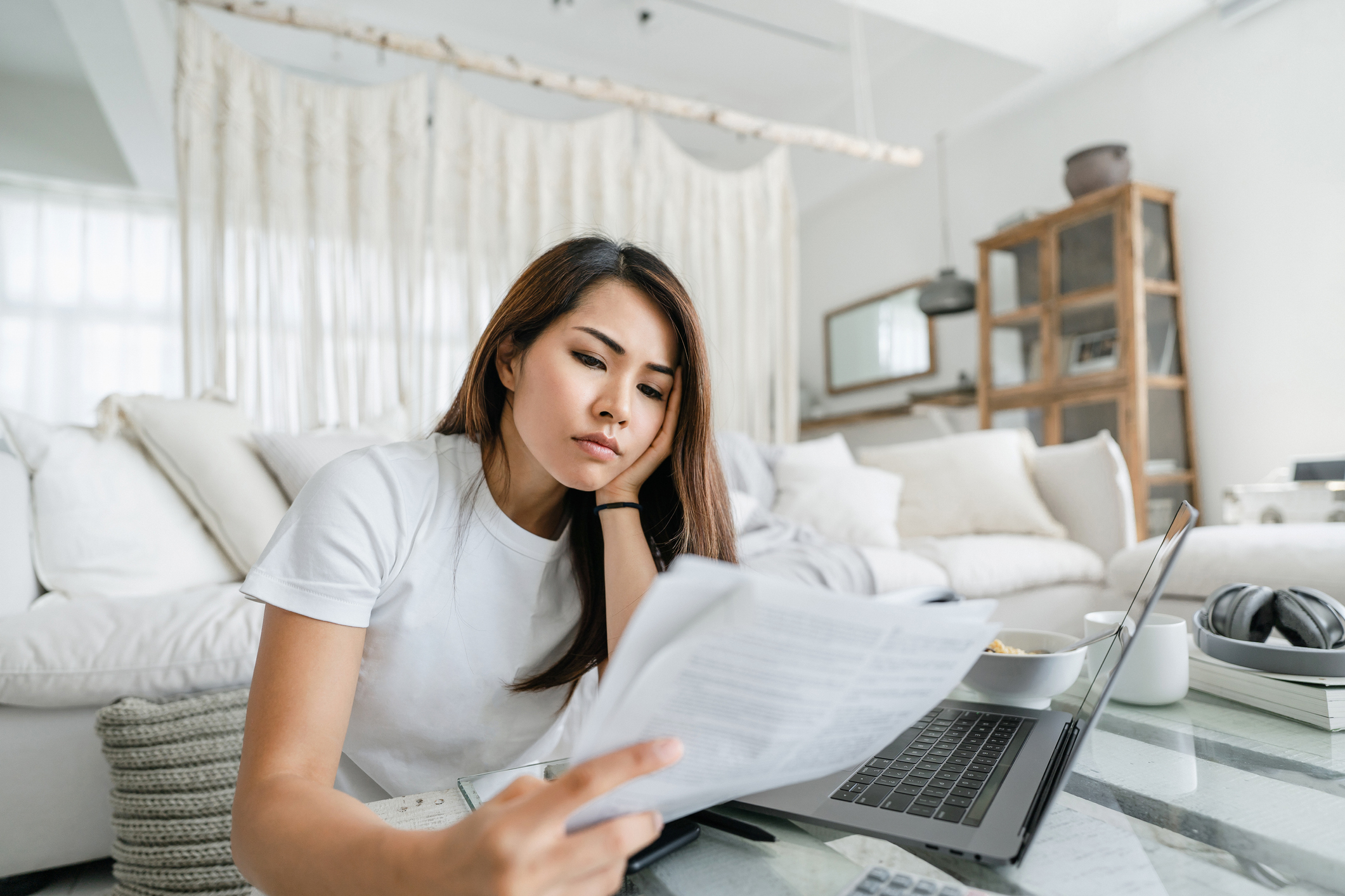 Worried young investor looks at paperwork in living room. Person looking worried while reviewing paperwork in living room.
