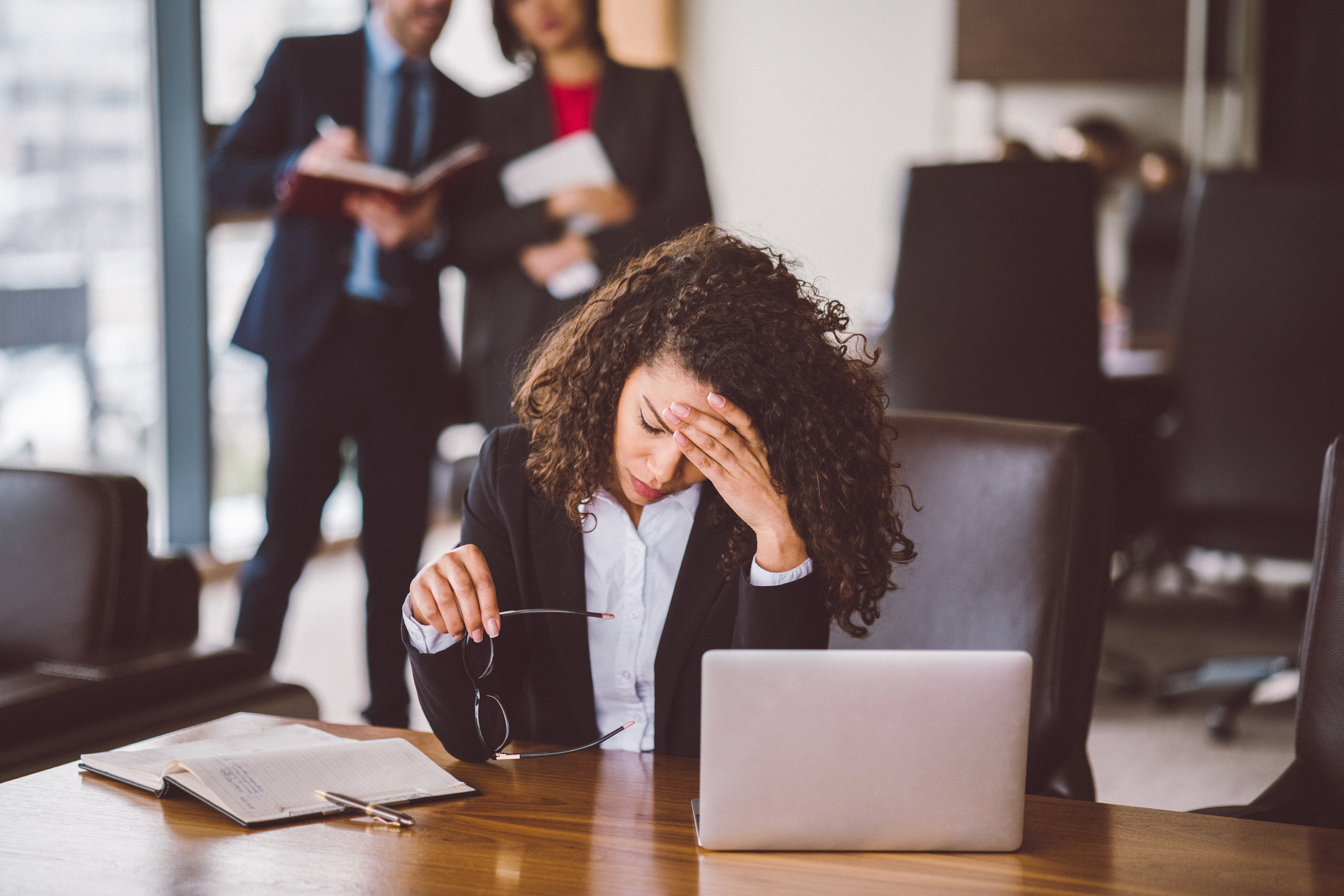 Businesswoman holding glasses and rubbing forehead worriedly.