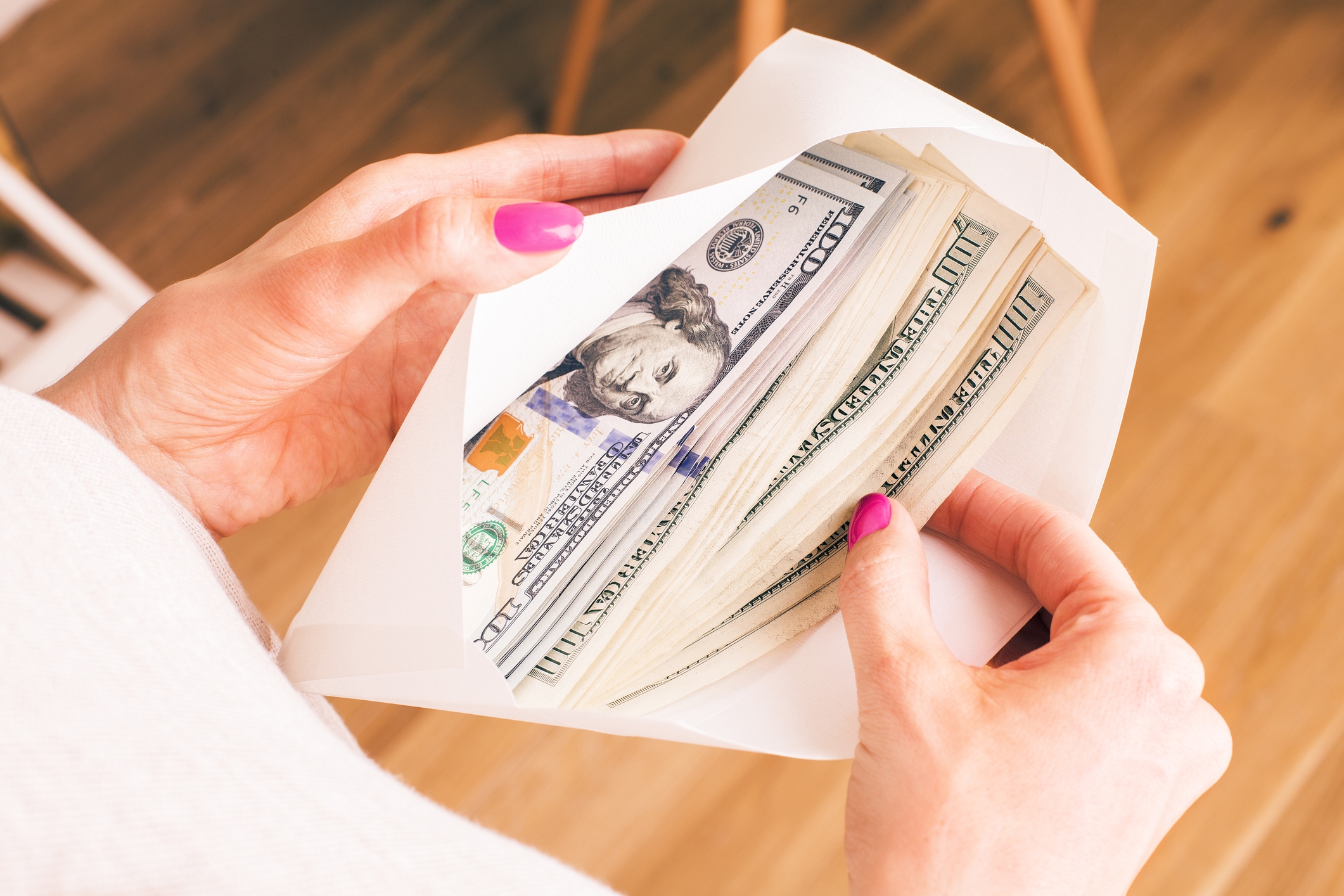 A person pulls hundred dollar bills from an envelope
