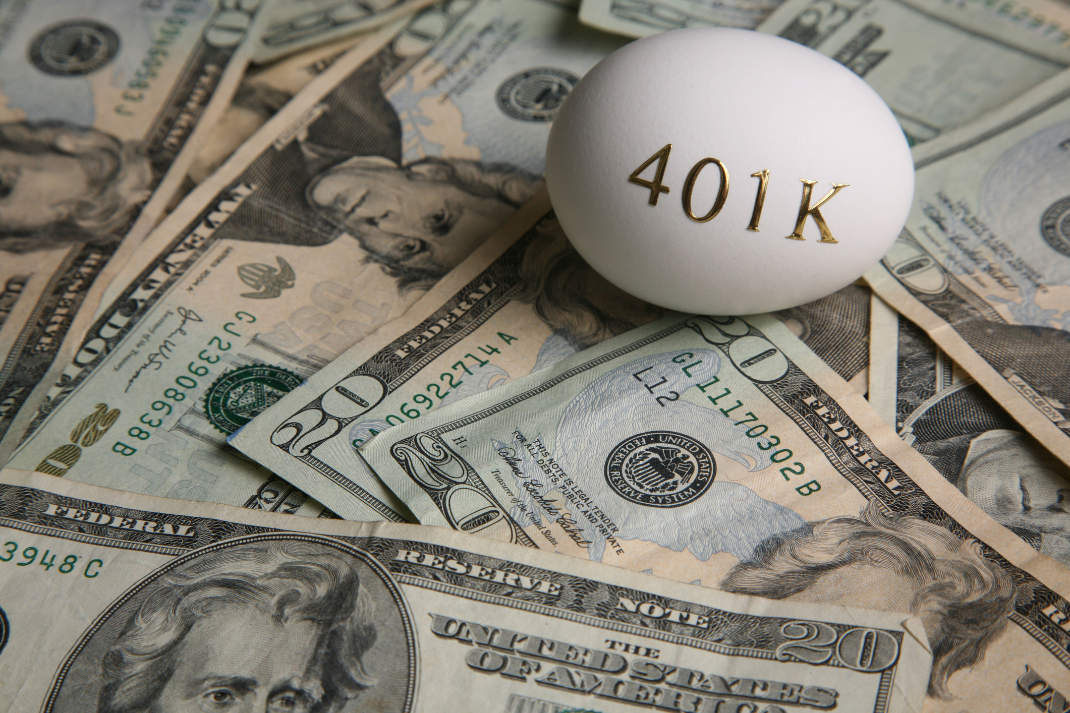 An egg with 401(k) written on it on top of a pile of cash An egg with 401(k) written on it on top of a pile of cash.
