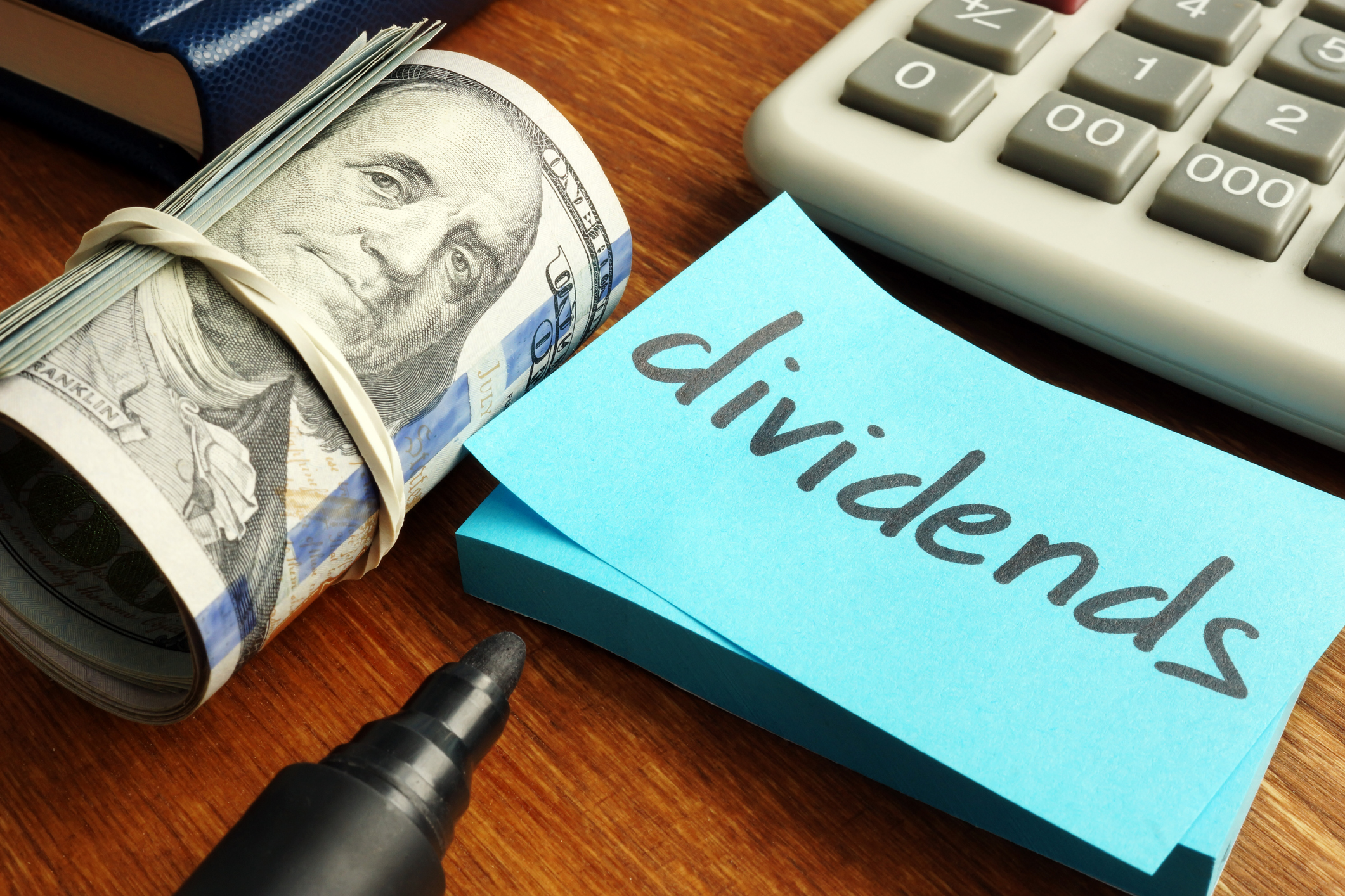 The word Dividends written on a piece of paper sitting next to a roll of cash