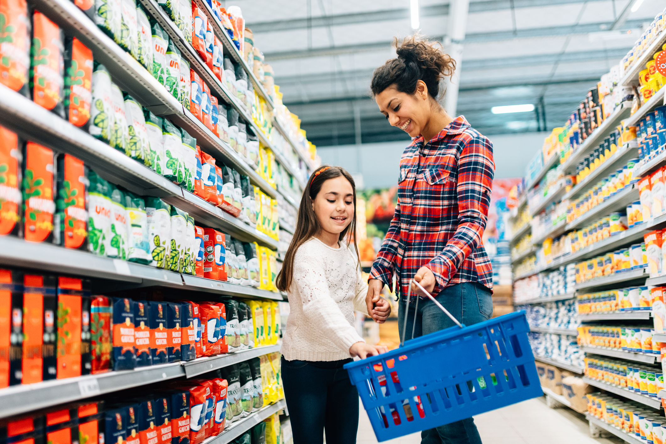 Mother and daughter browsing grocery aisle and placing items in blue shopping basket Parent and child browsing grocery aisle and placing items in blue shopping basket.