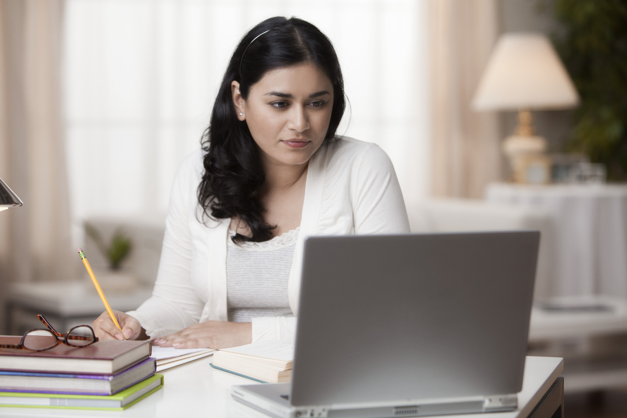 Person at laptop writing notes. Person at desk is looking at laptop and writing notes.