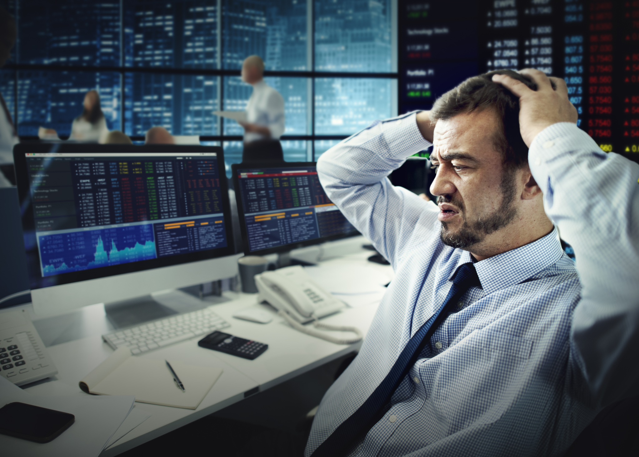 Stock trader losing money A trader looking at monitors in dismay with hands on head.