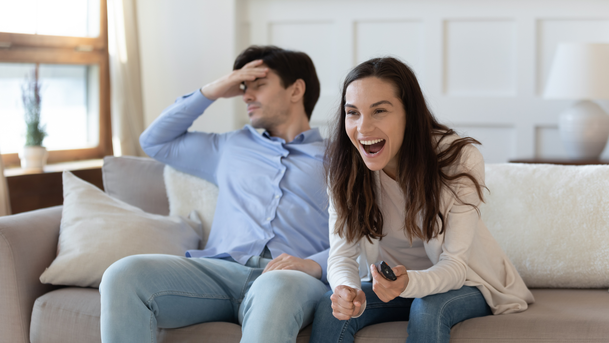 Excited and frustrated people sharing a TV couch Two people sharing a couch and displaying opposite emotions. One is excited, and the other is not.
