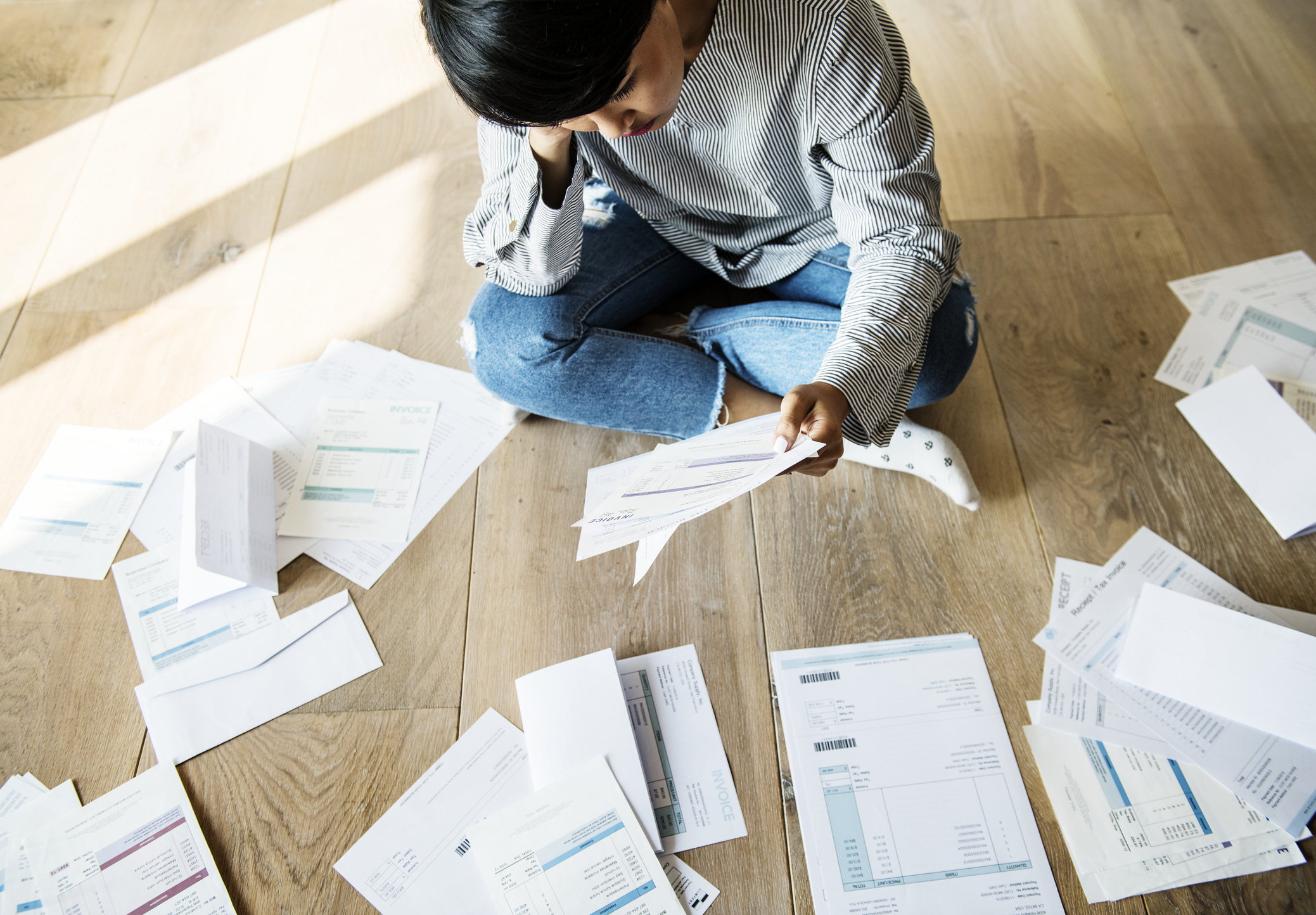 Woman on floor with bills spread out around her.