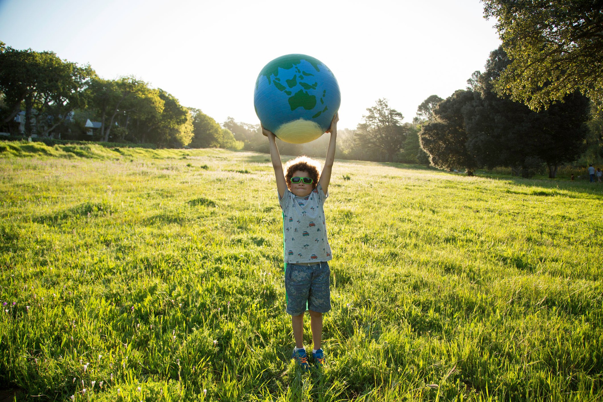 child_standing_holding_globe_outdoors Child standing outside holding a globe above their head.