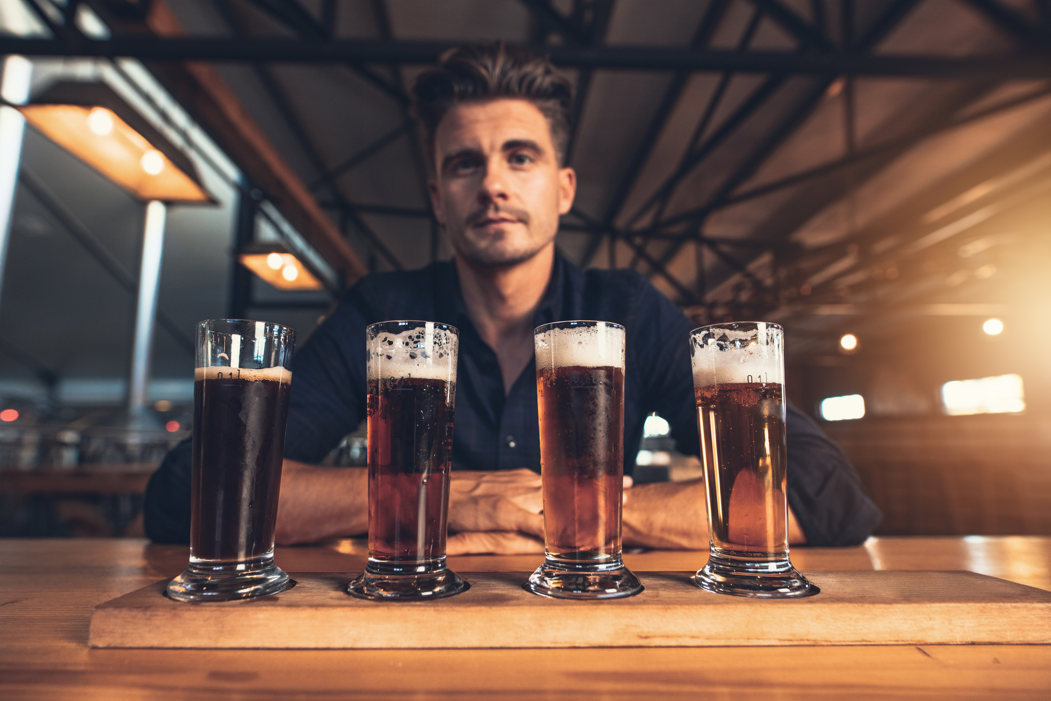A person sits in front of a flight of four different beers in pilsner glasses.