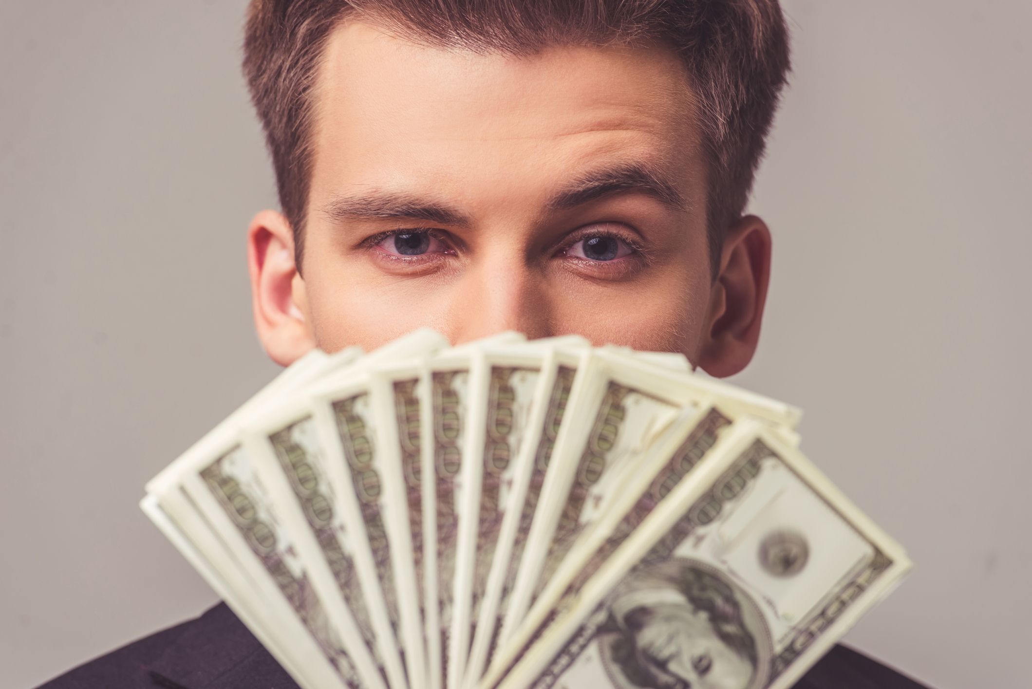 Person holding cash Person holding dollar bills up under their eyes.