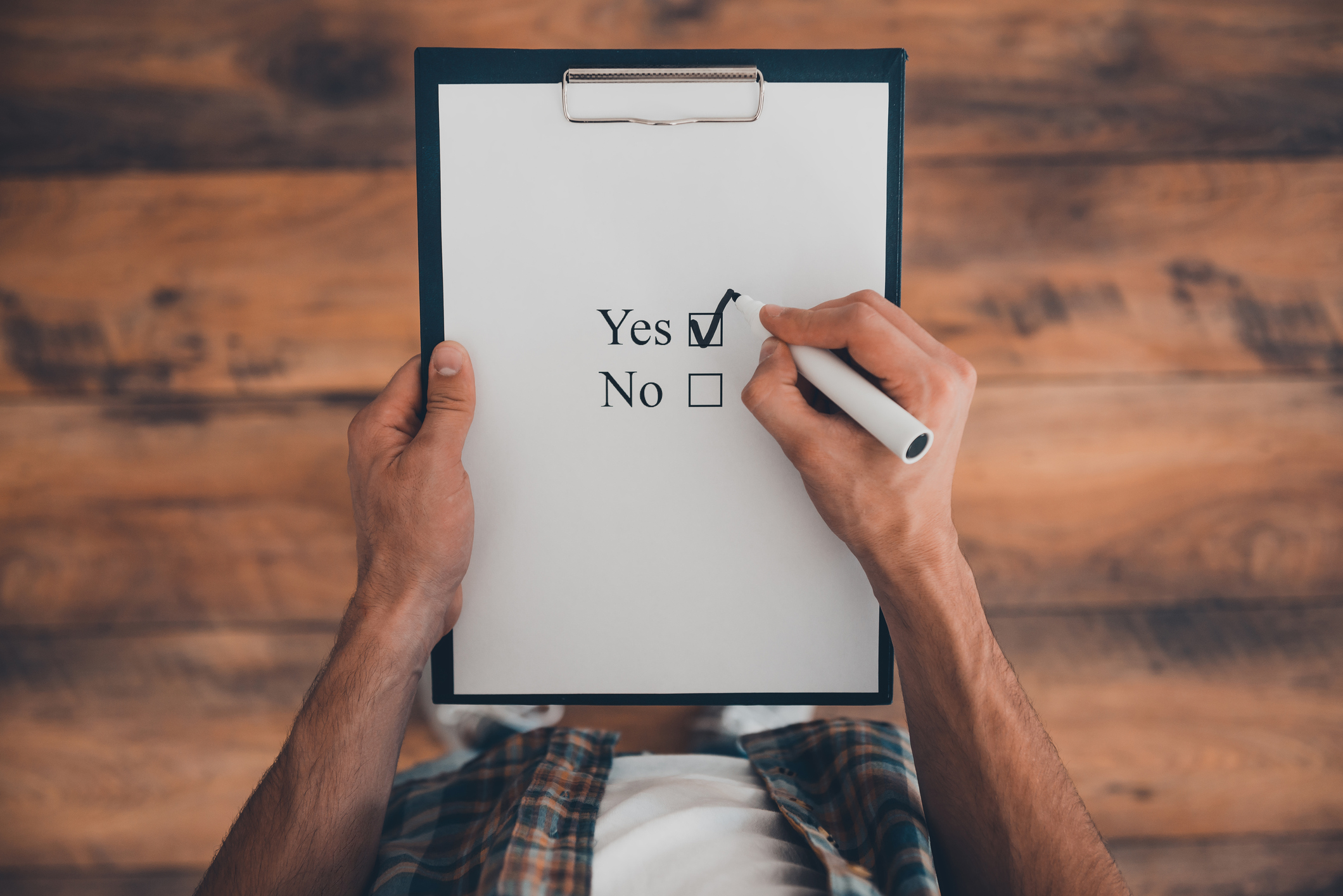 A piece of paper with yes and no check boxes and the yes box is checked A person holding a clipboard with a piece of paper that has yes and no check boxes with a check mark in the yes box.