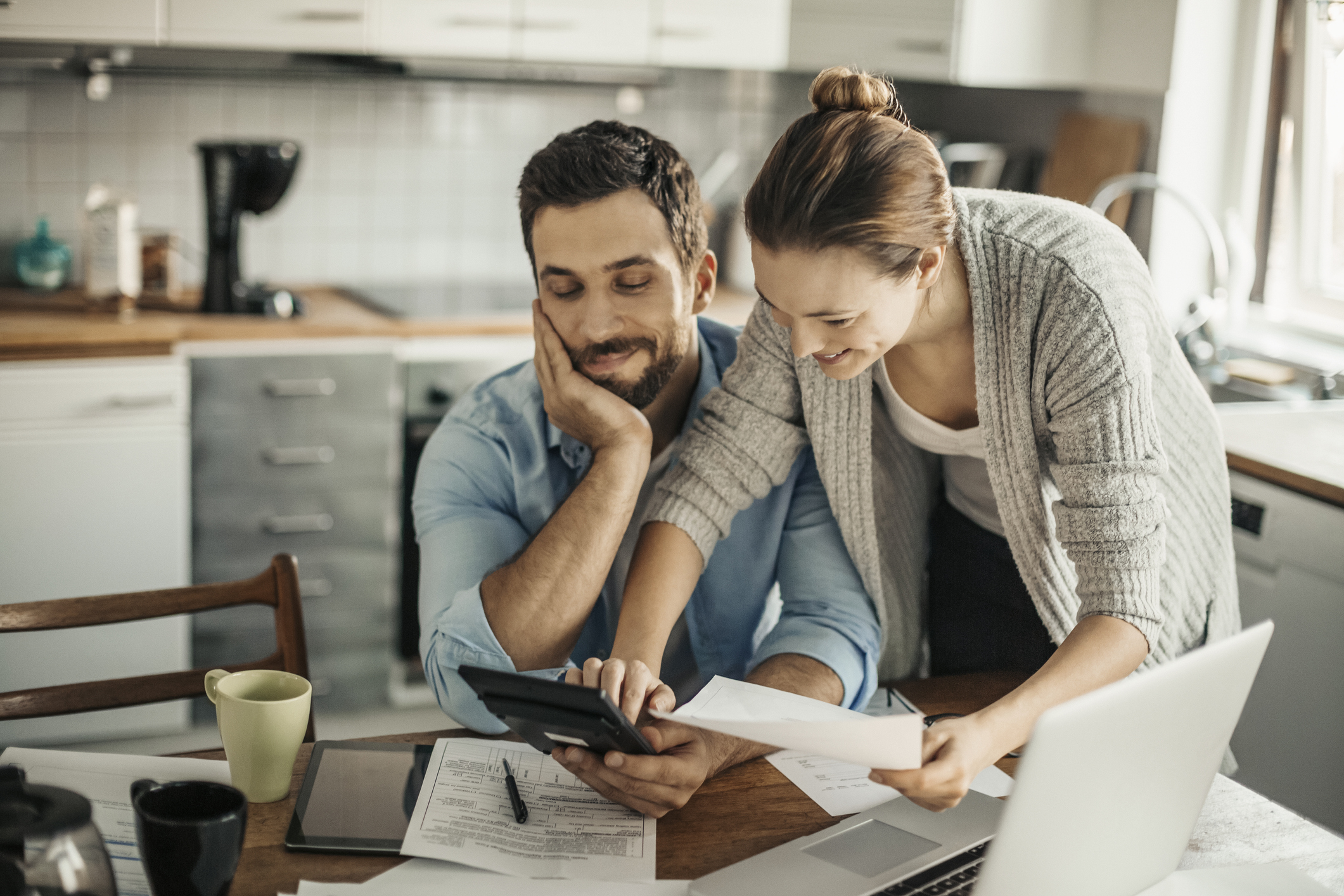 couple-checking-finances.jpg Two smiling people review paperwork at home in front of laptop.
