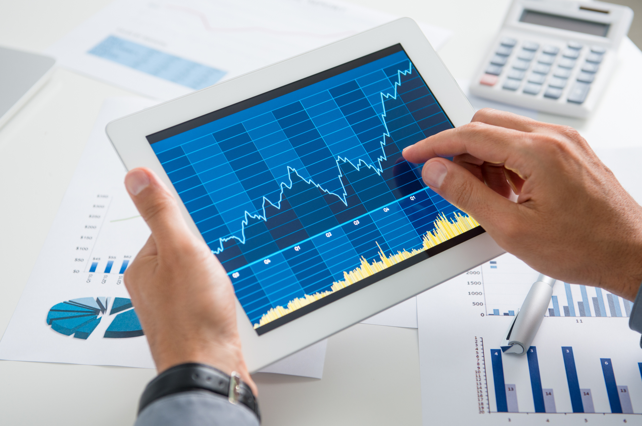 Hands holding a tablet and inspecting a line graph on its screen.