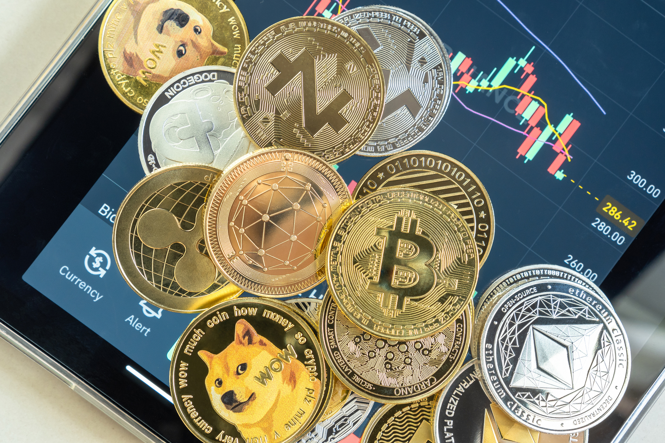 crypto_token_image Different cryptocurrencies lying in a pile atop a smartphone opened to a trading app.