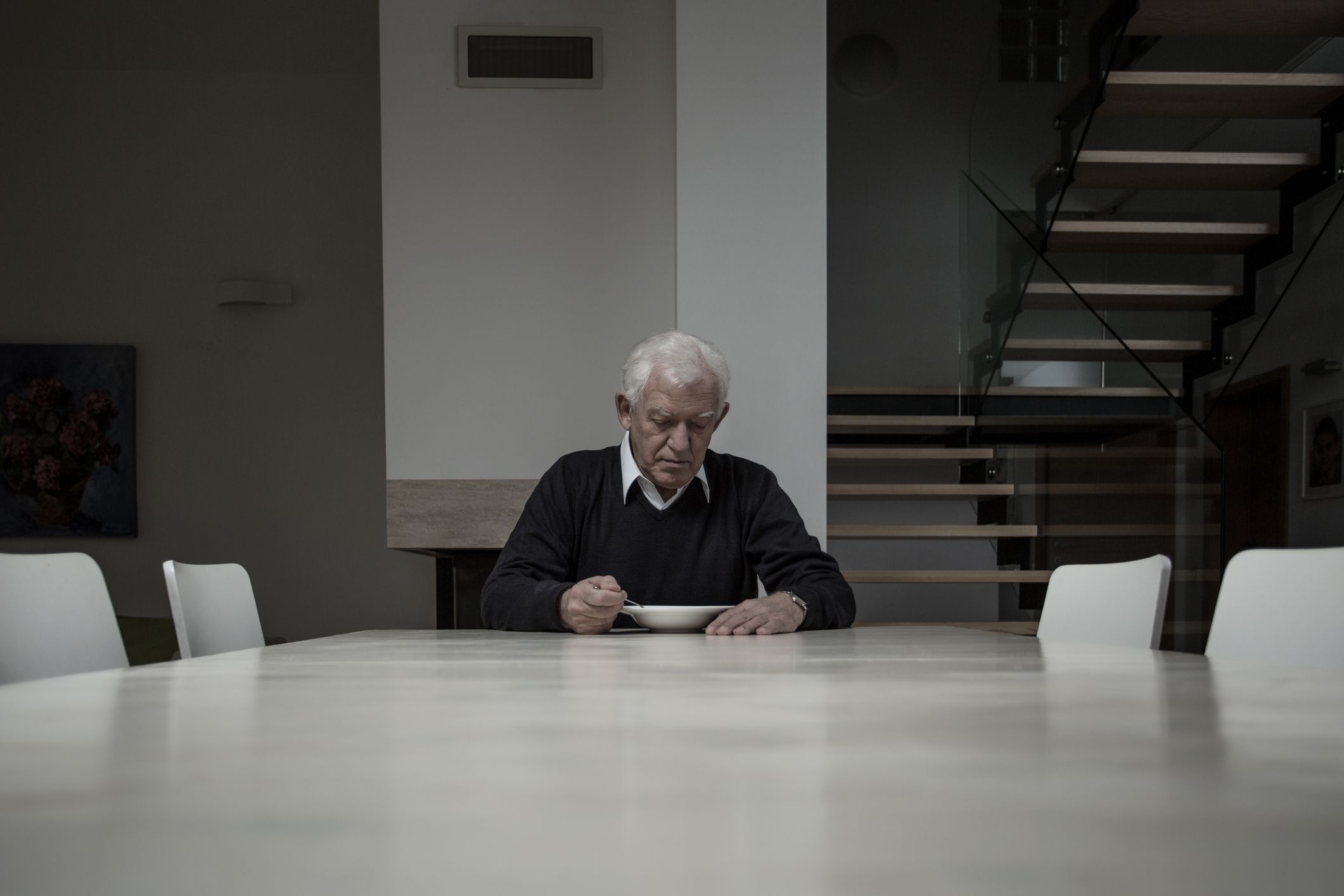 elderly person sitting alone at large table in gray house and eating from a bowl -- senior lonely loneliness sad