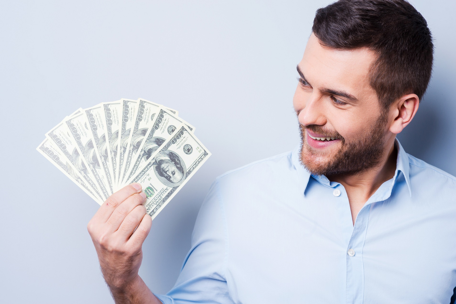 Man holding a fanned pile of hundred dollar bills while smiling.
