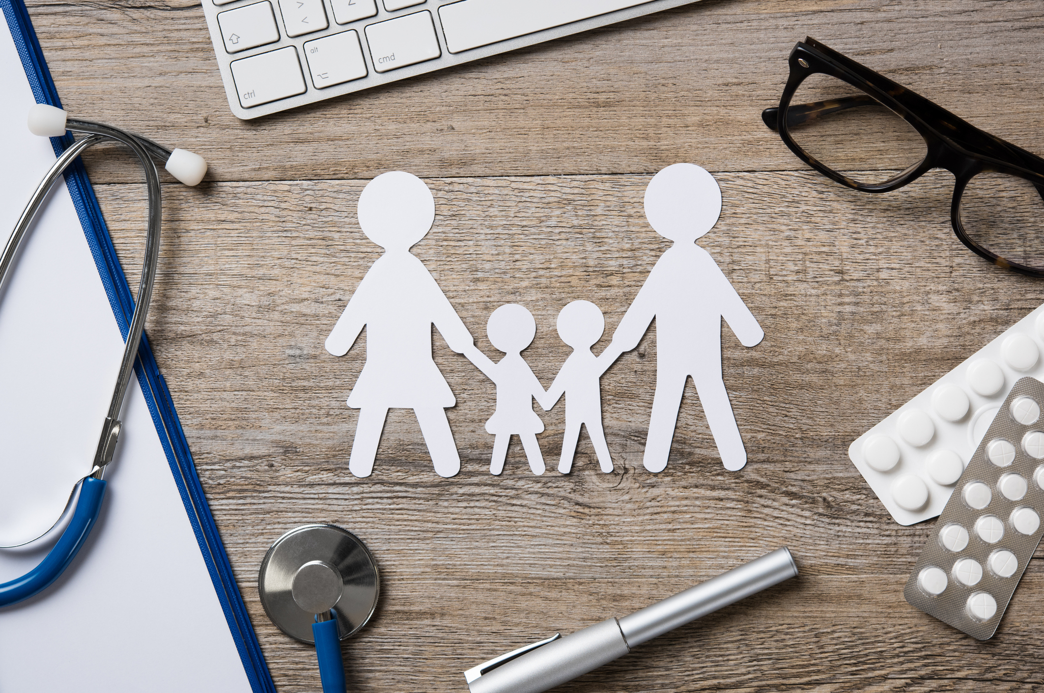 Paper cutout of family next to stethoscope, pills, and glasses.