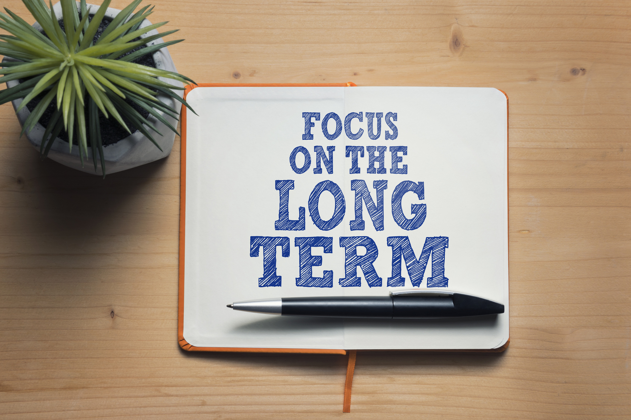 Sign saying Focus on the Long Term A notebook with a pen lying across it opened to a page that says focus on the long term.