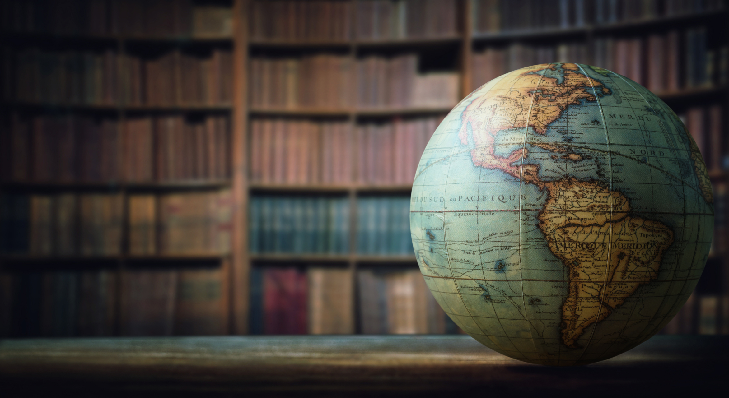 A globe on a table in front of a bookcase.